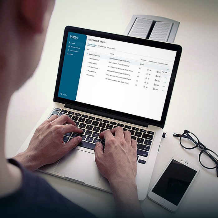A view over the should of a man operating the Voqa managed backend support system on a laptop with a pair glasses and a mobile phone next to it
