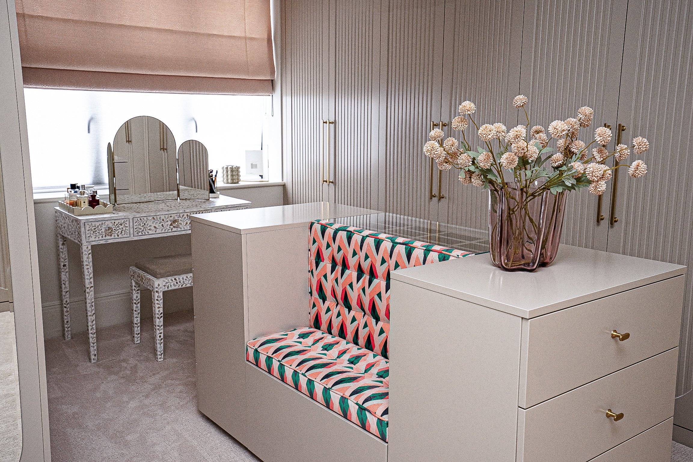 Chic dressing room with a colorful patterned bench, ornate vanity table, and a vase of flowers.