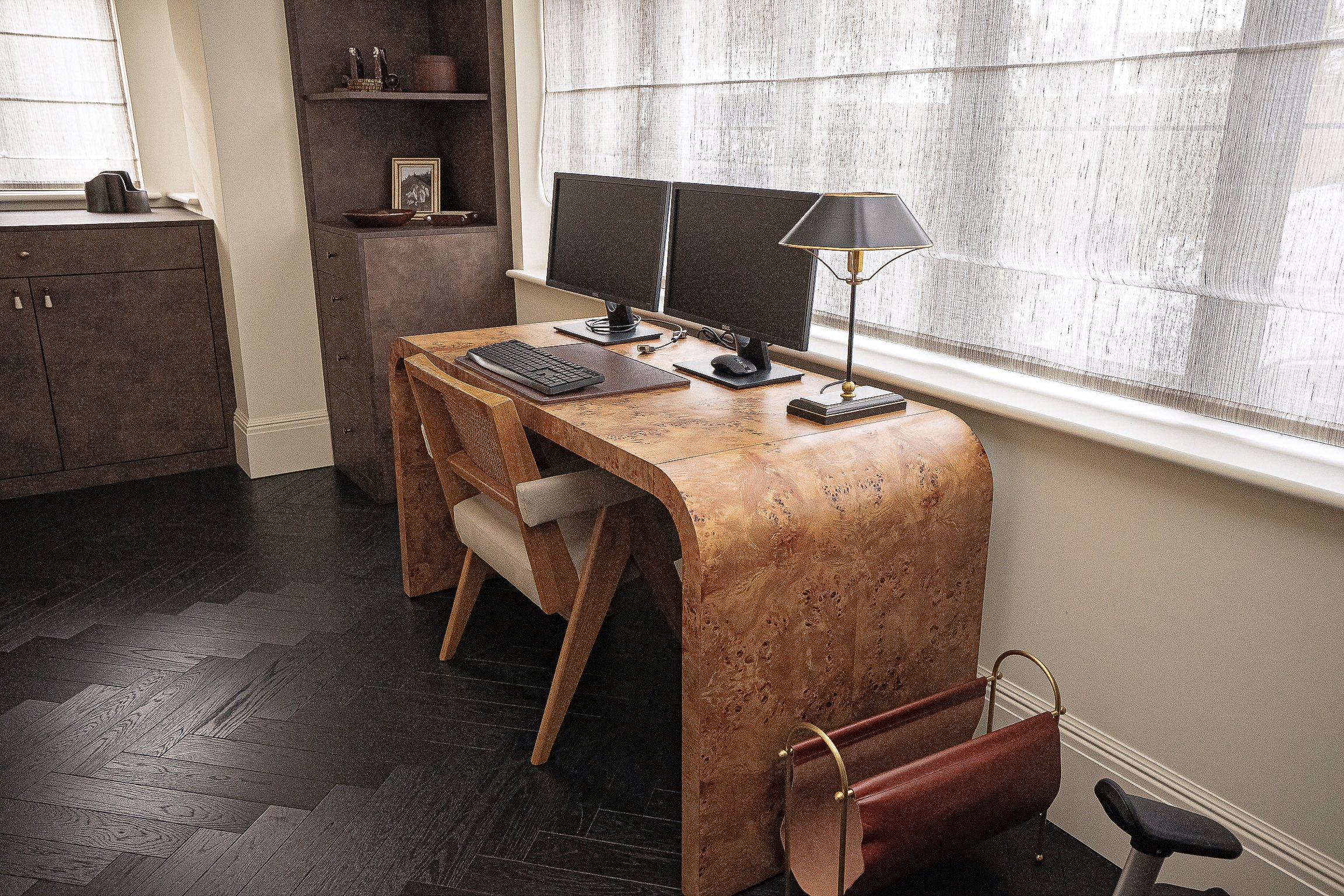 Modern home office with wooden desk, dual monitors, lamp, and chair.
