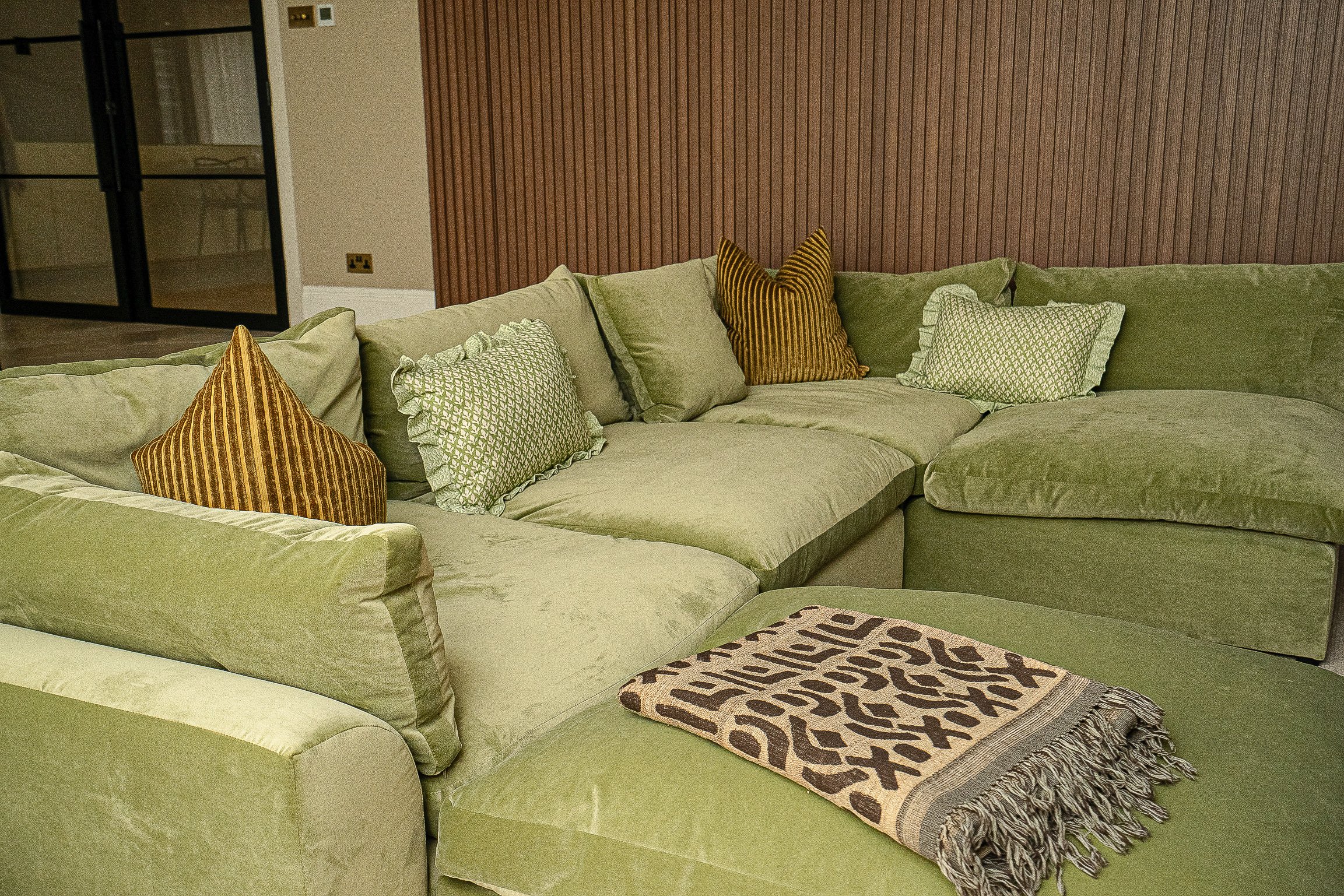 Green sectional sofa with assorted pillows and a patterned throw blanket in a living room.