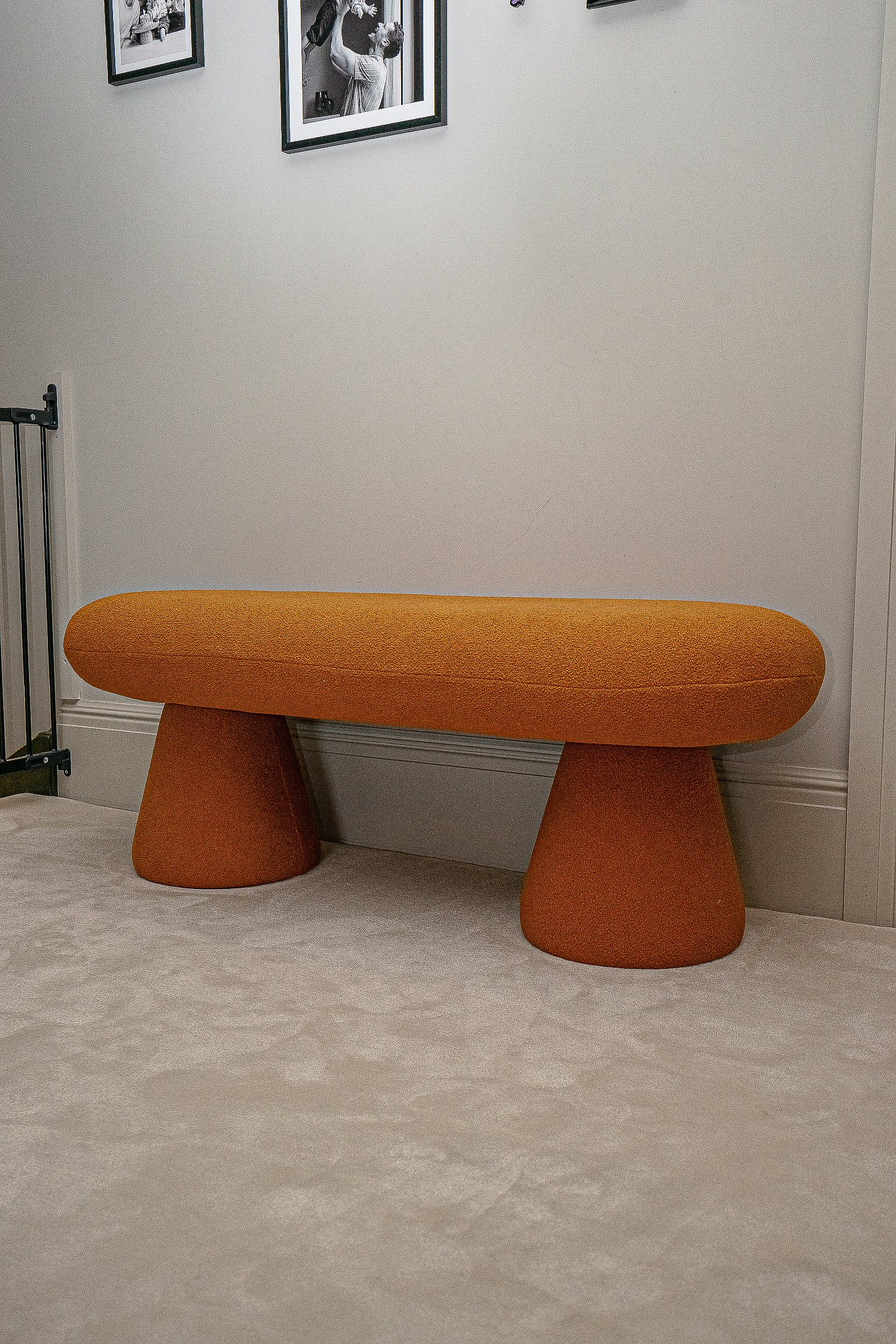 Orange bench with conical legs in a room with framed photos on the wall.
