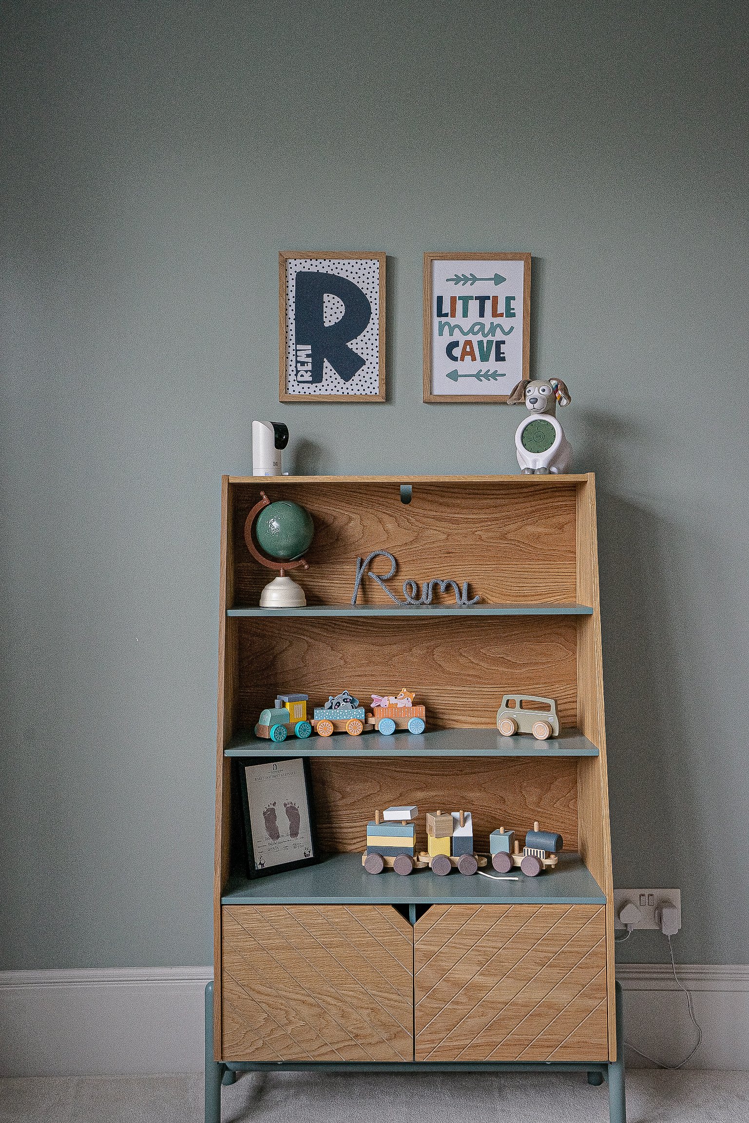 Wooden shelf with toy trains, a small globe, and framed prints on the wall. A dog-shaped clock is on top of the shelf.