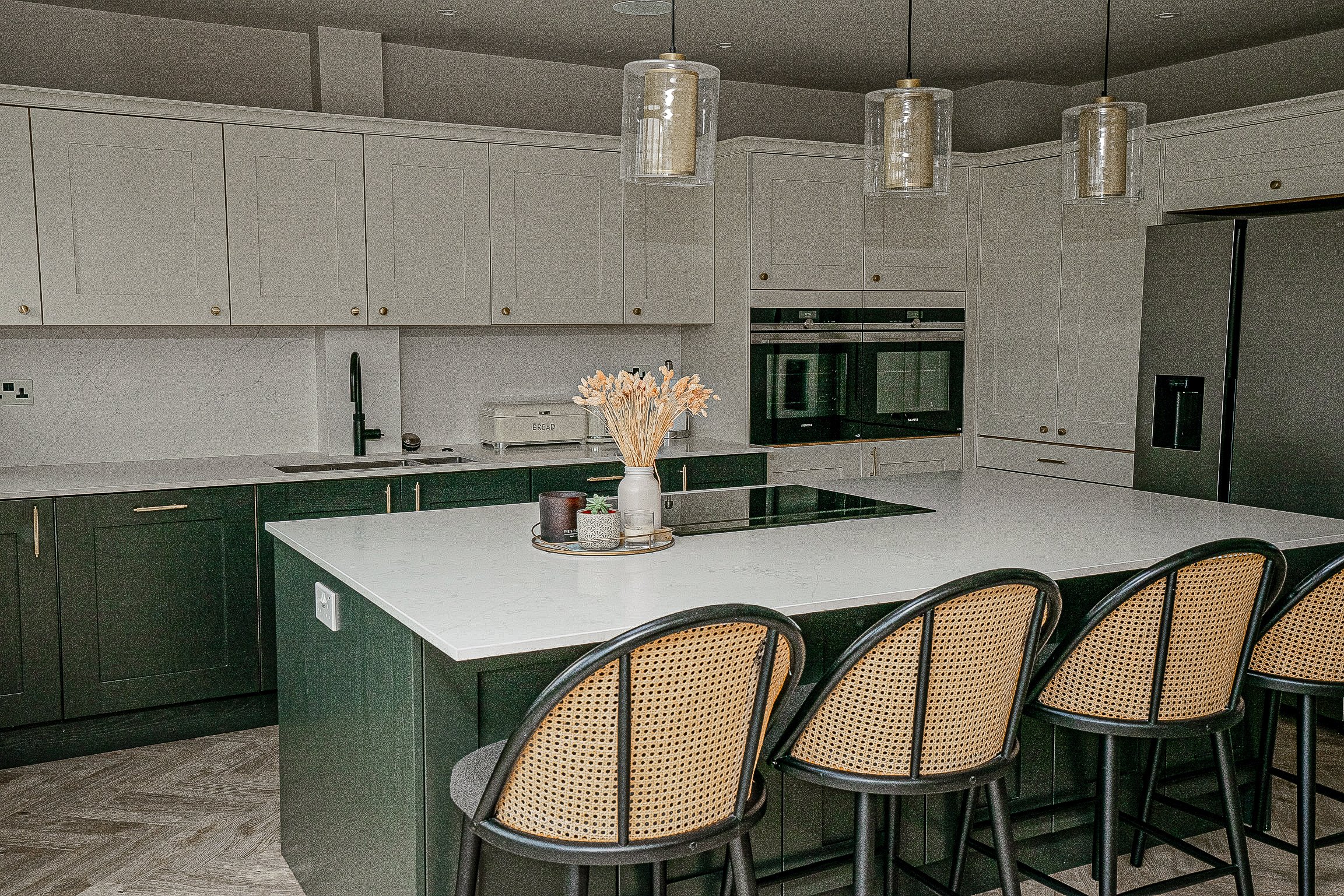 Modern kitchen with white and green cabinets, large island, bar stools, pendant lights, stainless steel appliances, and decor items.