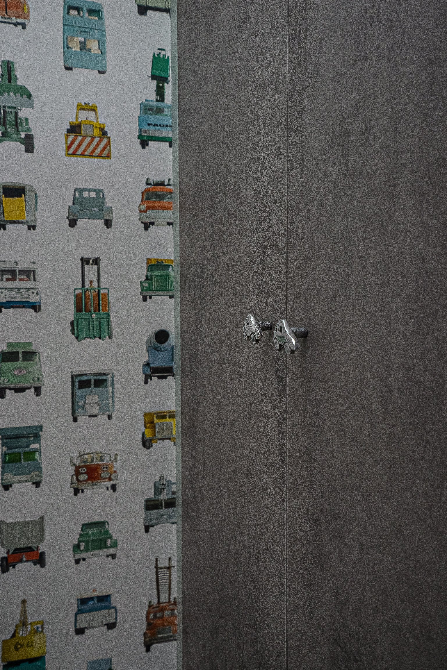 Gray paneled wall with car-themed wallpaper featuring colorful cartoon vehicles on the left.