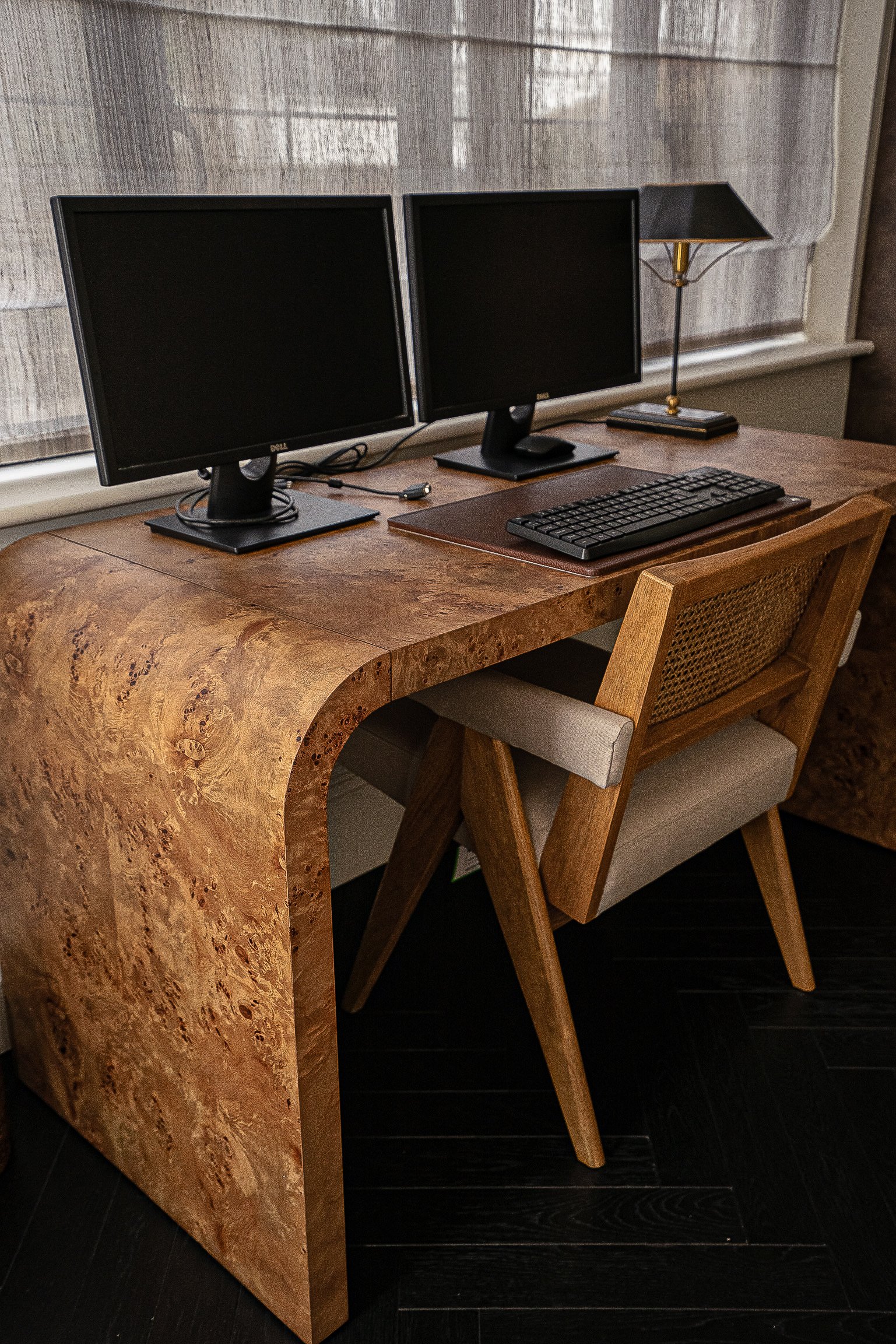 Wooden desk with two computer monitors, keyboard, and desk lamp