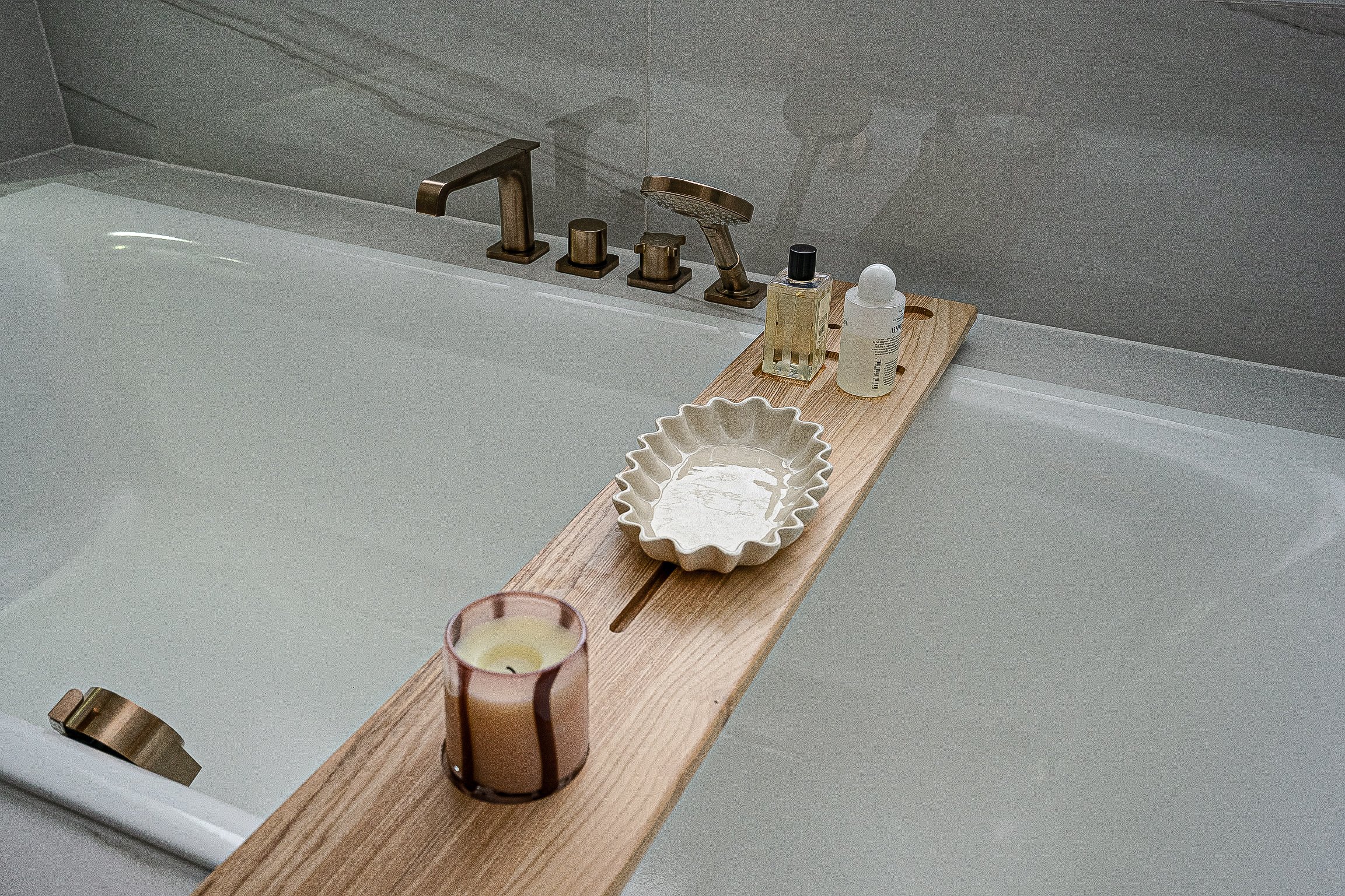 Bathtub with wooden tray holding a candle, soap dish, and bath products