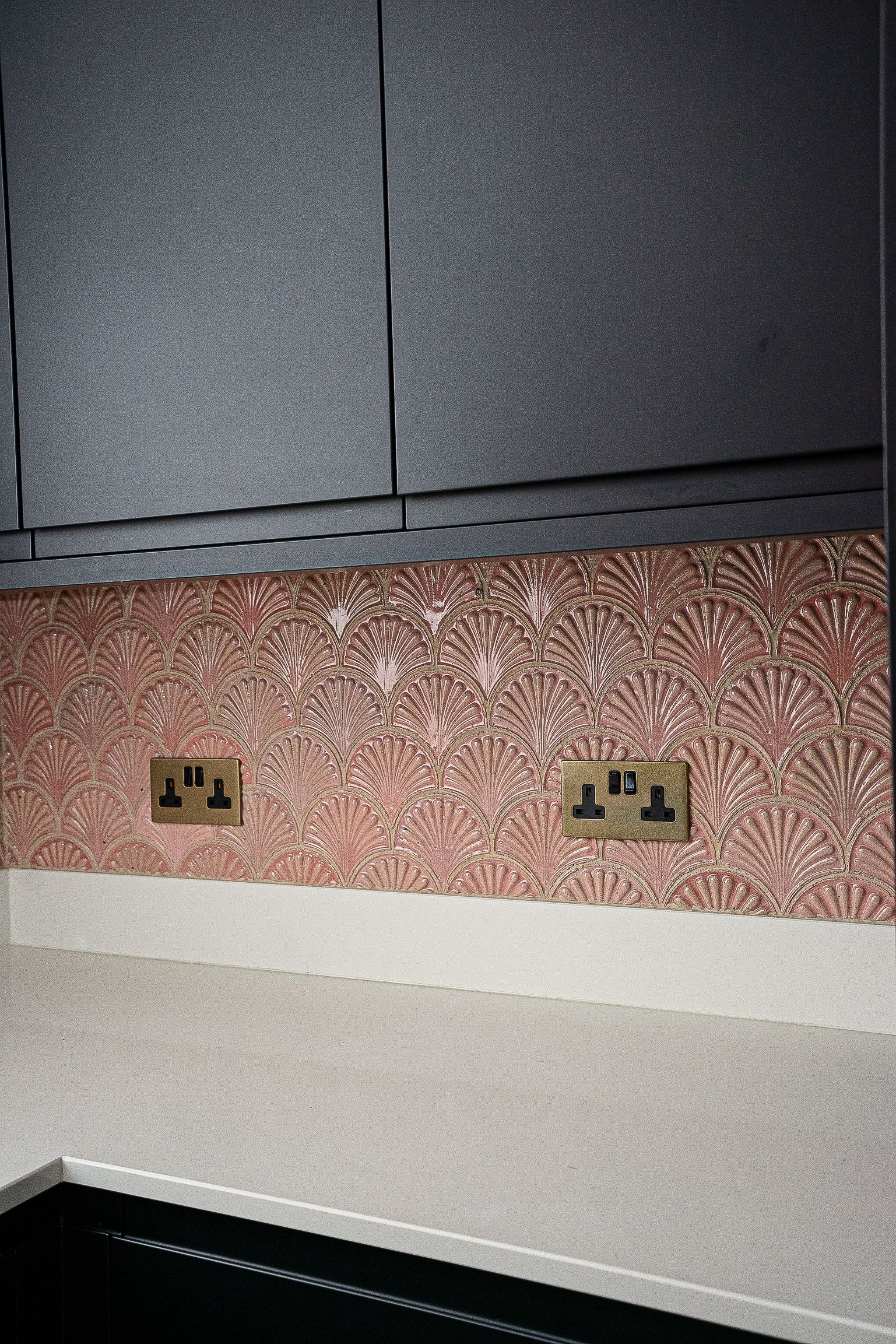 Kitchen countertop with black cabinets, pink scallop-patterned backsplash, and wall outlets.