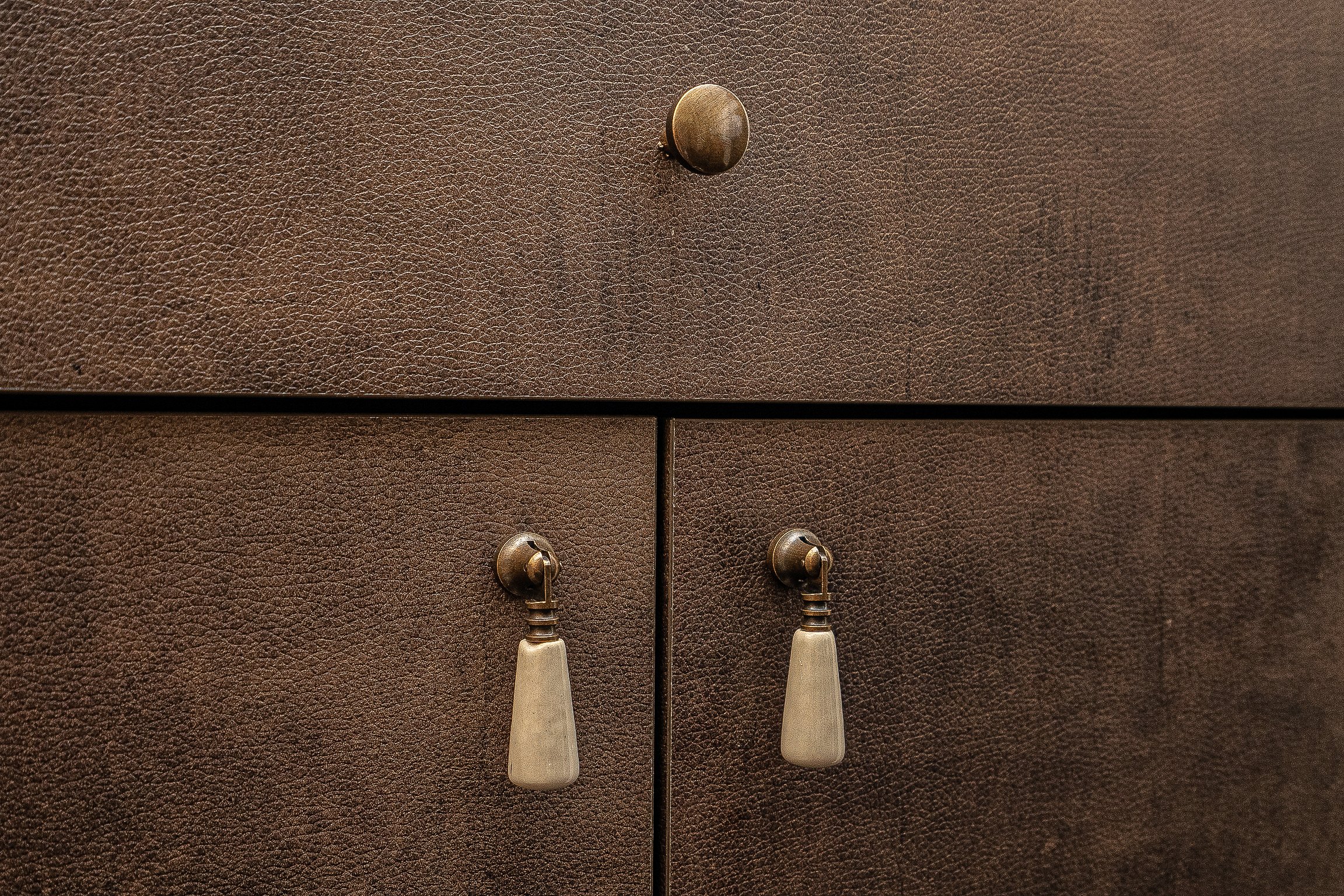 Close-up of textured brown drawers with three brass handles, one round and two pendant-style