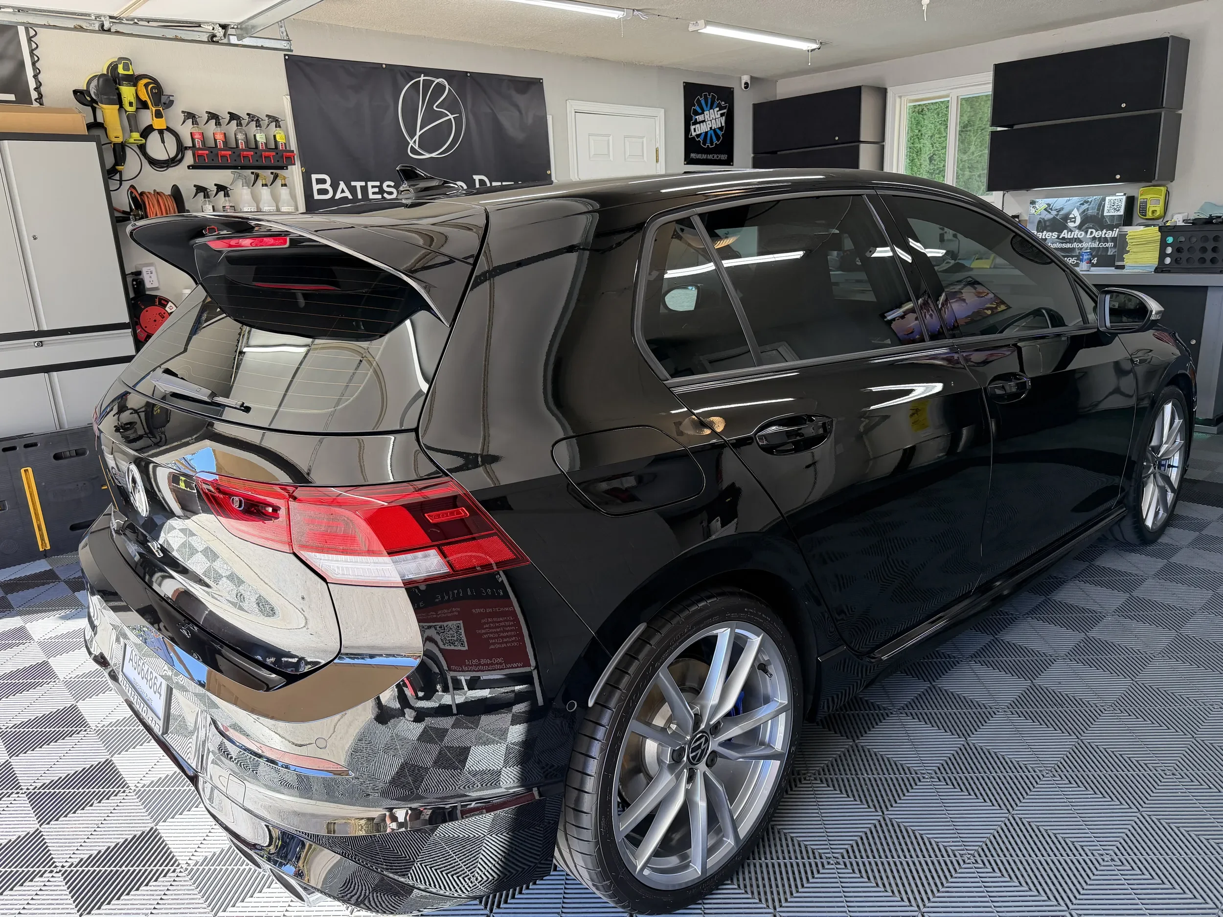 Rear three-quarter view of a glossy black Volkswagen Golf after detailing in a clean garage.
