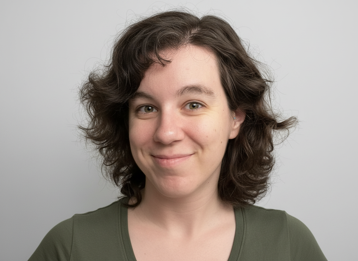 A young woman with short, curly brown hair and light skin, smiling slightly, wearing a dark green top against a plain light gray background.