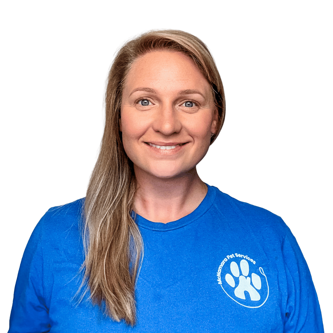 A woman with long blonde hair, wearing a blue t-shirt with the logo 'McNamara Pet Services' displayed on it, smiling and looking at the camera.