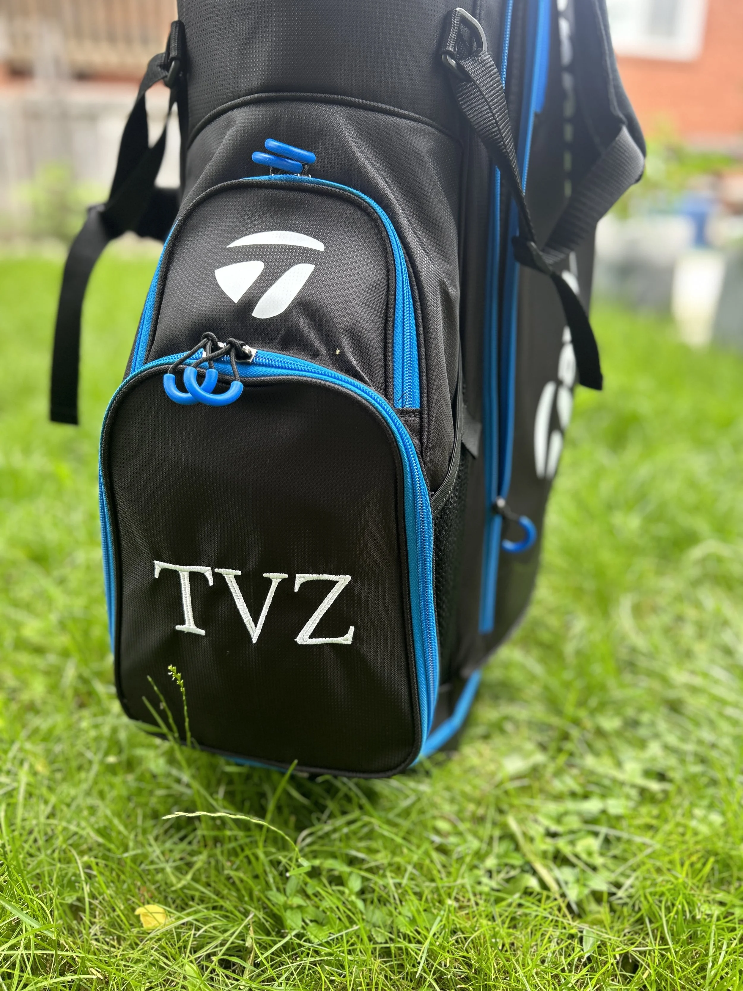 Black and blue golf bag on green grass with TVZ embroidered on the front pocket.