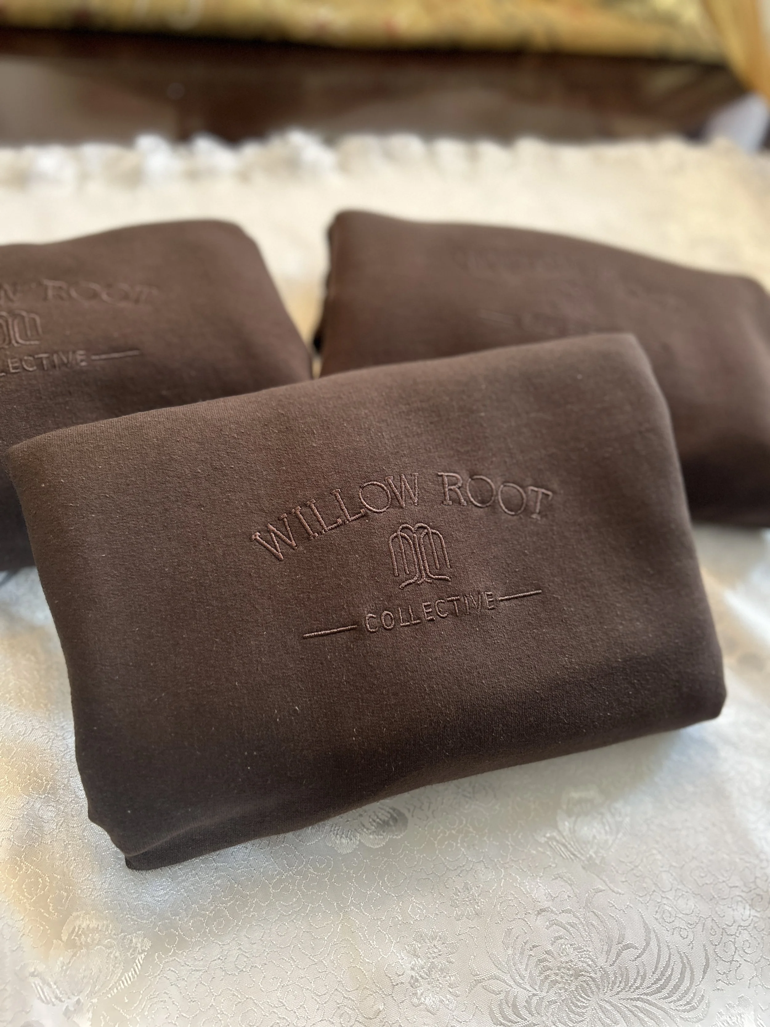 Three brown cloth bags with embossed 'WILLOW ROOT COLLECTIVE' logo resting on a cream-colored textured fabric surface.