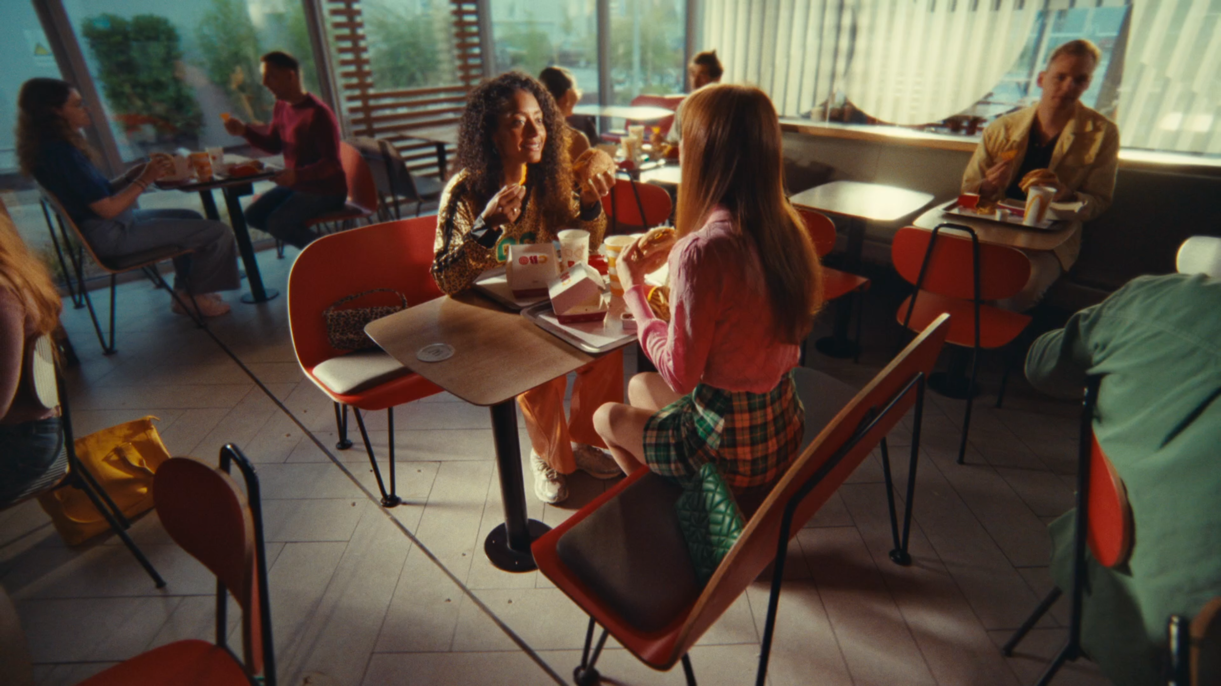People eating at tables in a fast food restaurant with large windows and natural lighting.