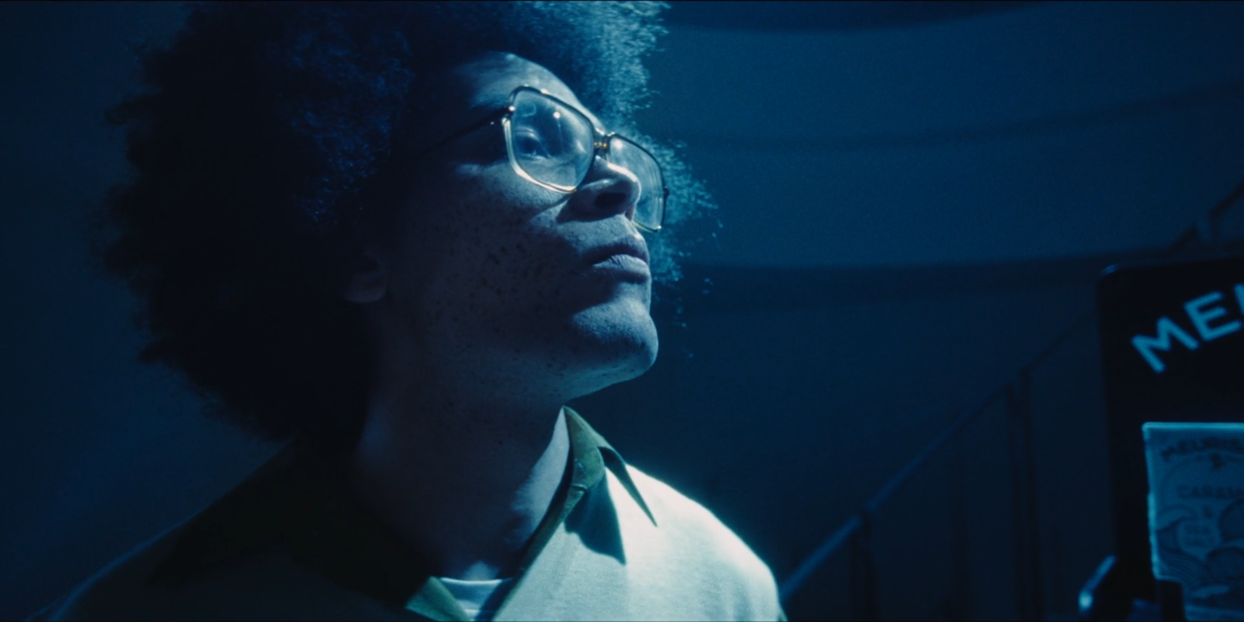 A person with glasses and curly hair underwater, looking upward in a tank or underwater environment.