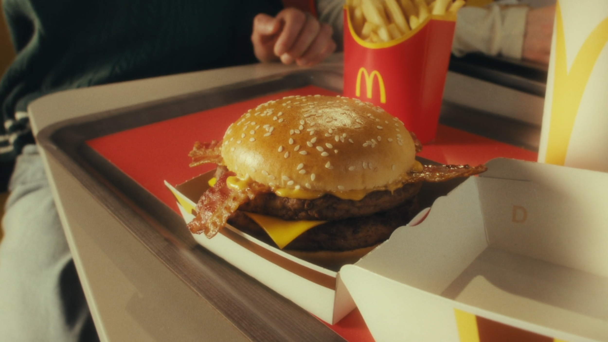 McDonald's cheeseburger with bacon, cheese, beef patty, sesame seed bun, served with fries in a red container, on a McDonald's tray.