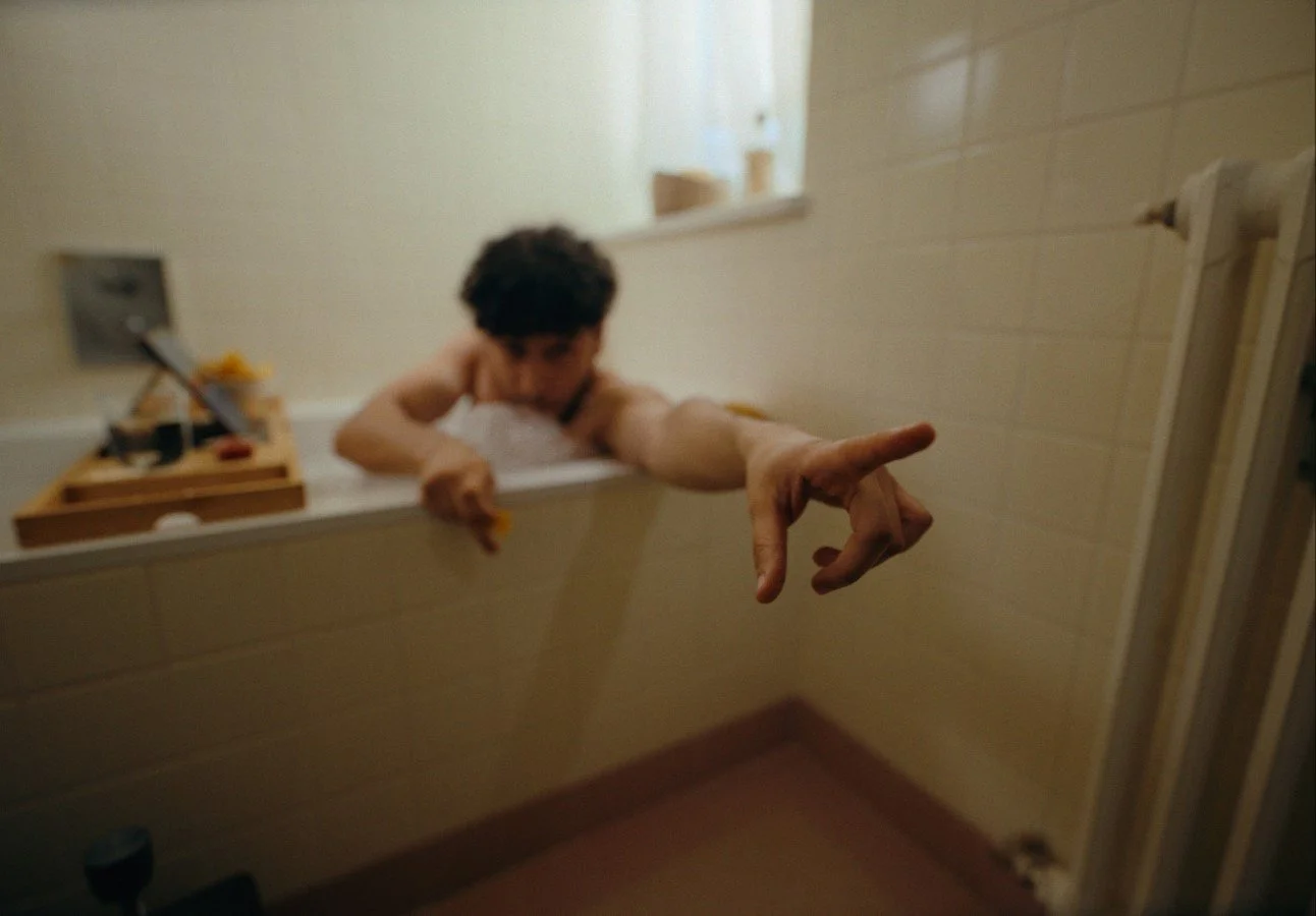 Person reaching out from a bathtub with blurred background and a window.