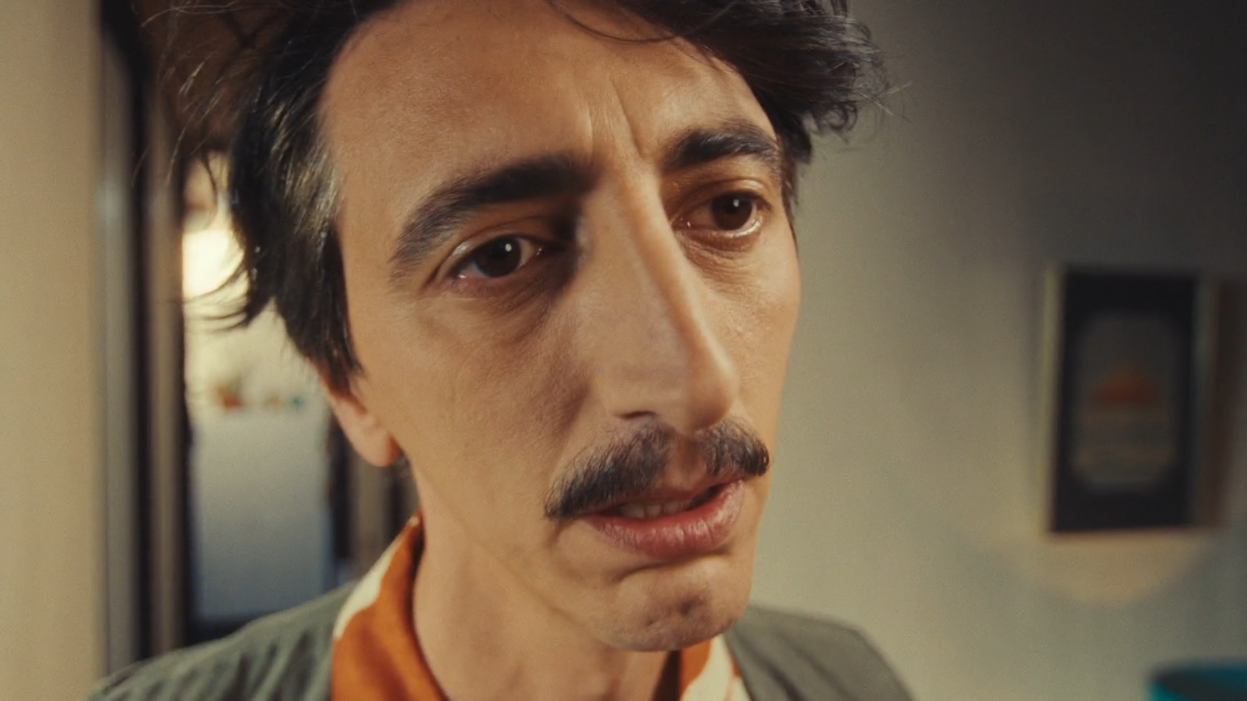 Close-up of a man's face with dark hair, mustache, and expressive eyes, looking slightly to the side.