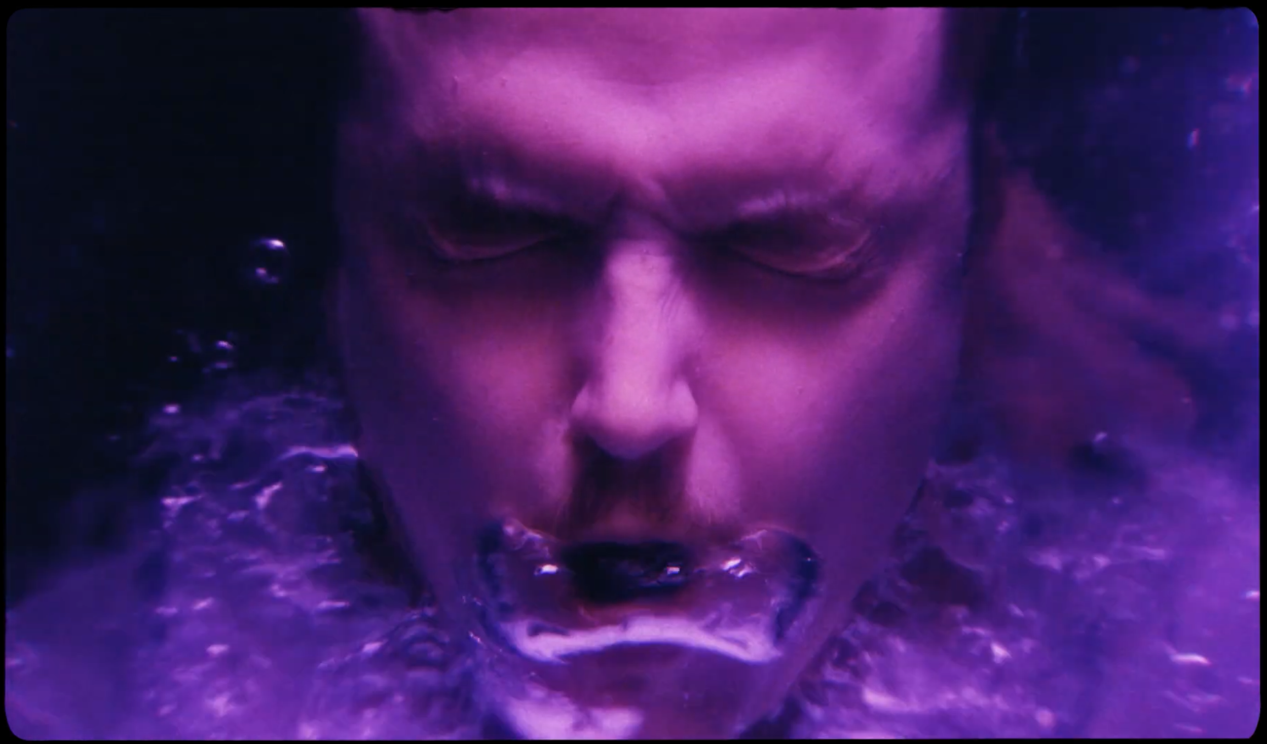 Close-up of a man's face with eyes closed, surrounded by swirling purple and black water, creating an intense and dramatic atmosphere.