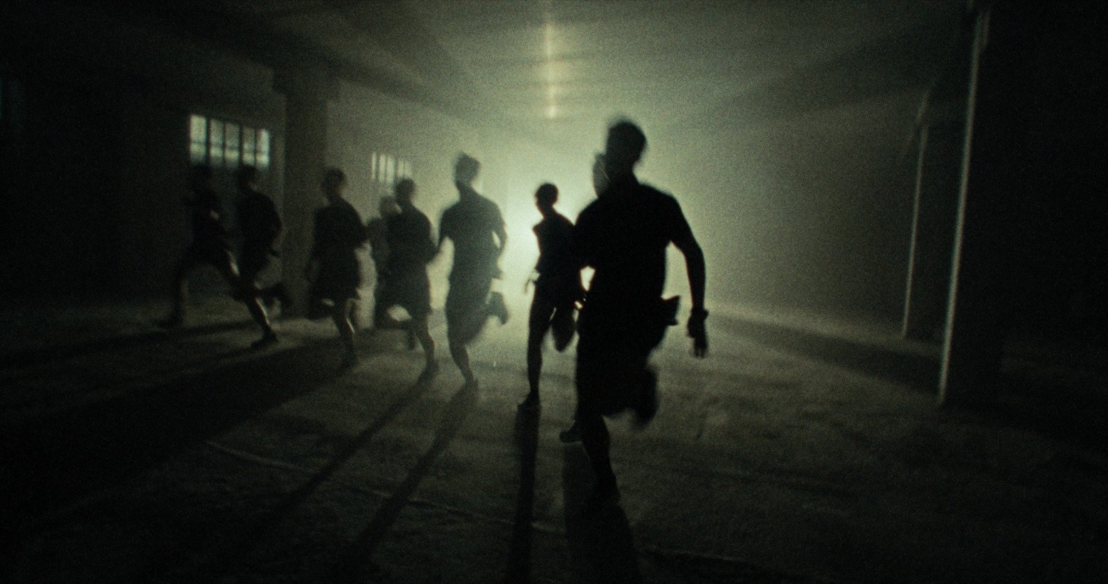 Group of children running indoors in a dimly lit room with windows, shadows cast on the floor.