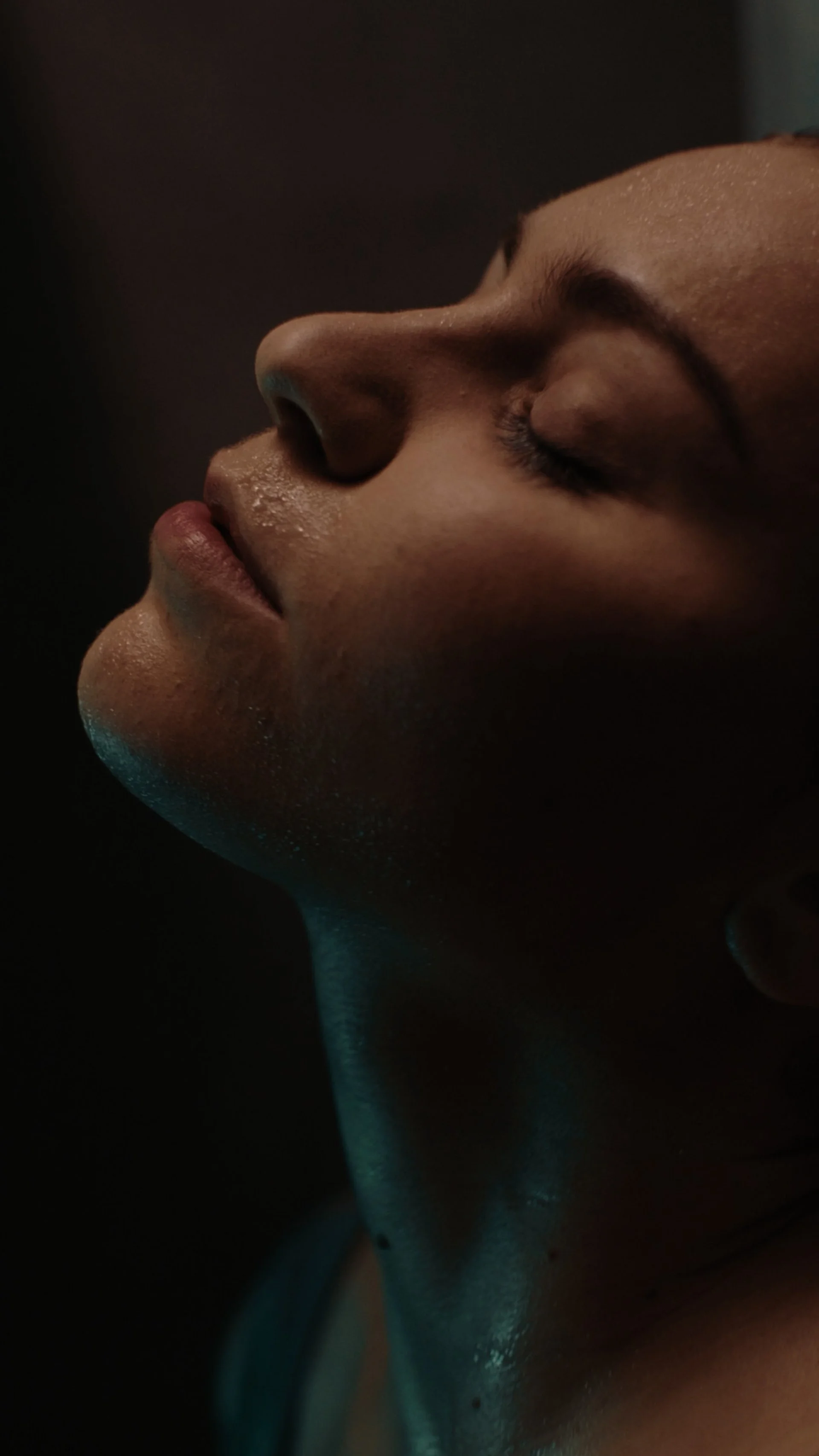 Close-up side profile of a woman's face with closed eyes, softly lit, showing her nose, lips, and smooth skin.