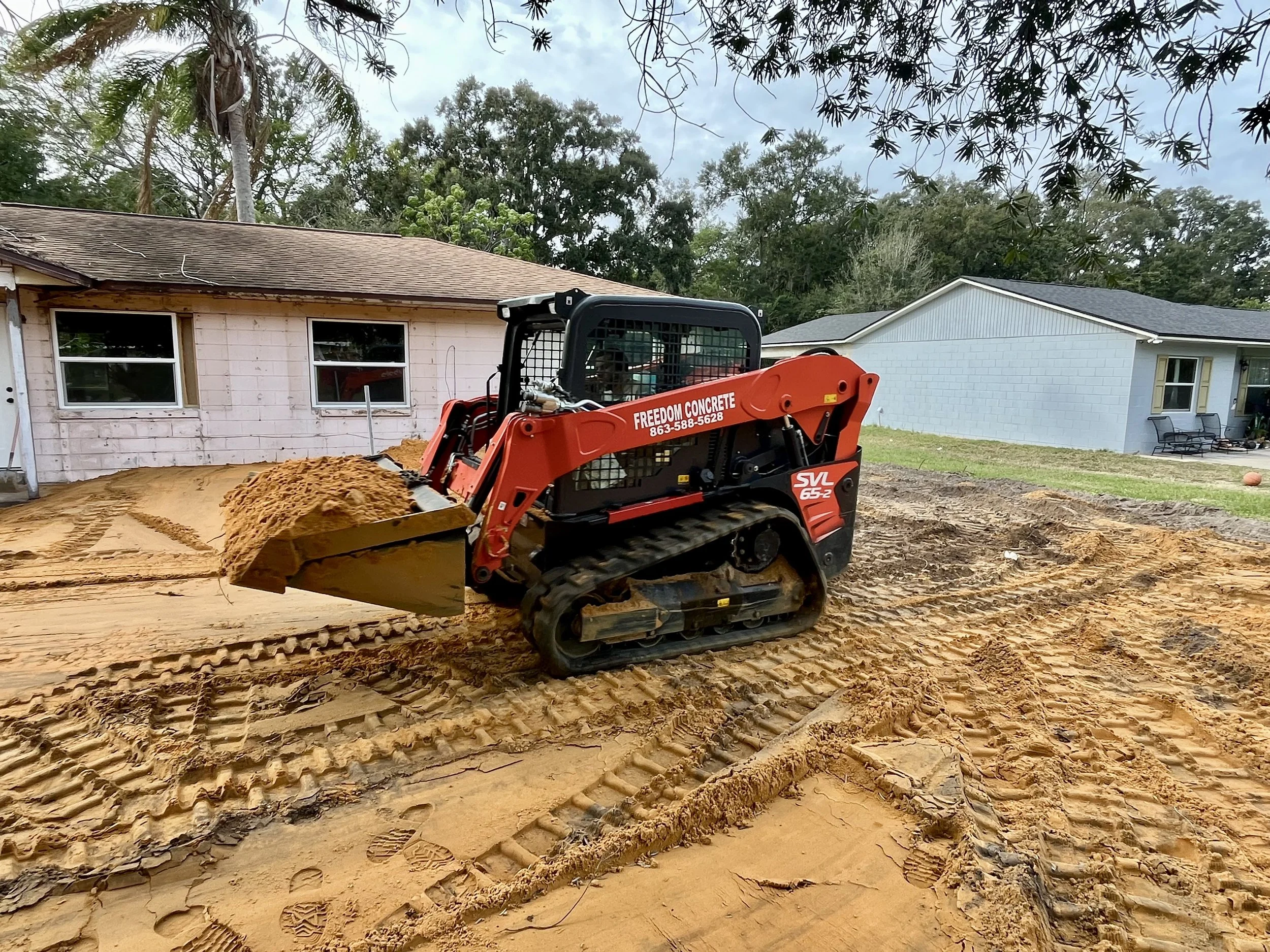 Freedom Concrete red skid steer grading sub-base dirt for concrete pad in Davenport FL