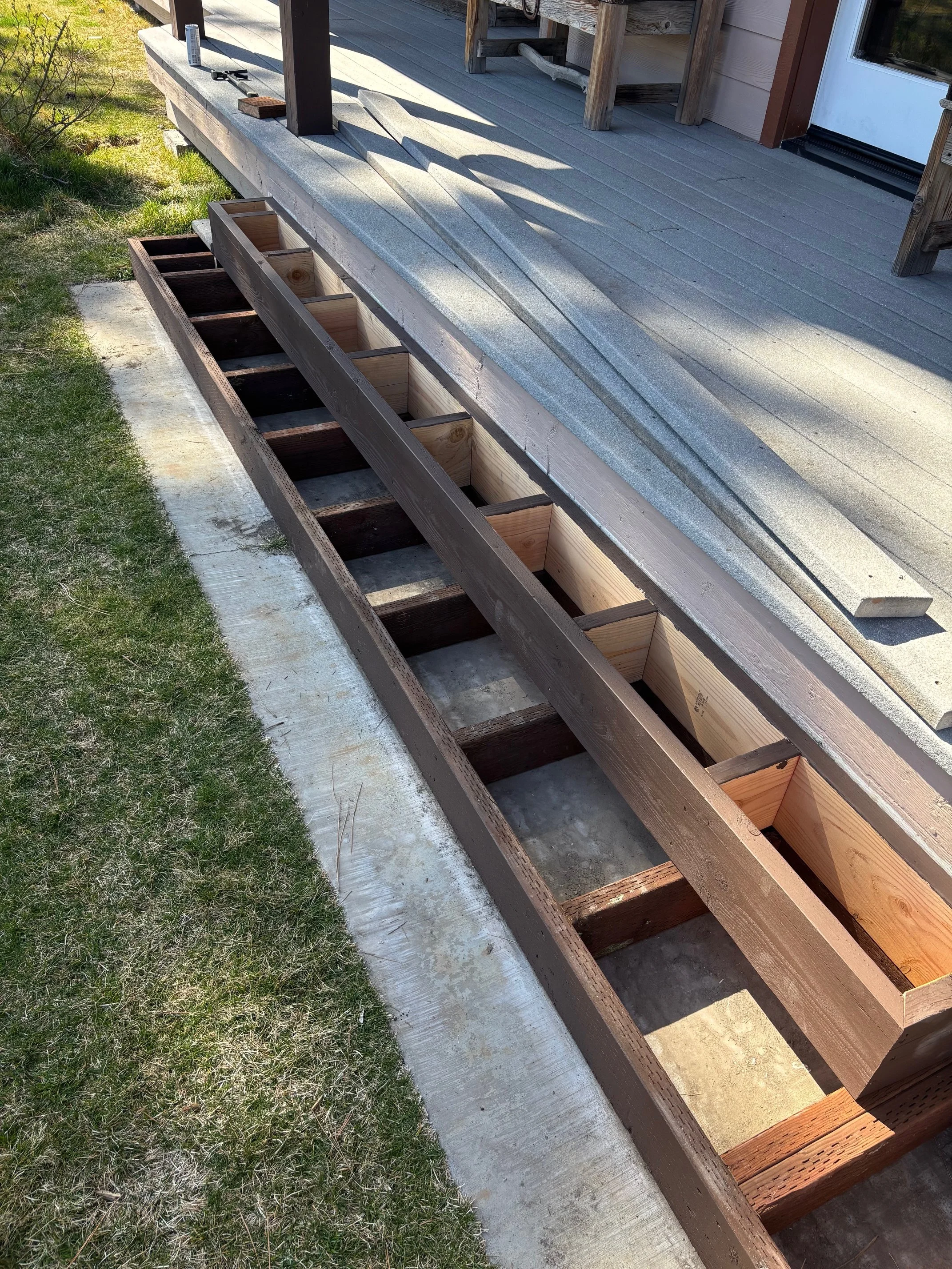 Wooden steps and planter box being built on a porch, with a grassy lawn beside it.