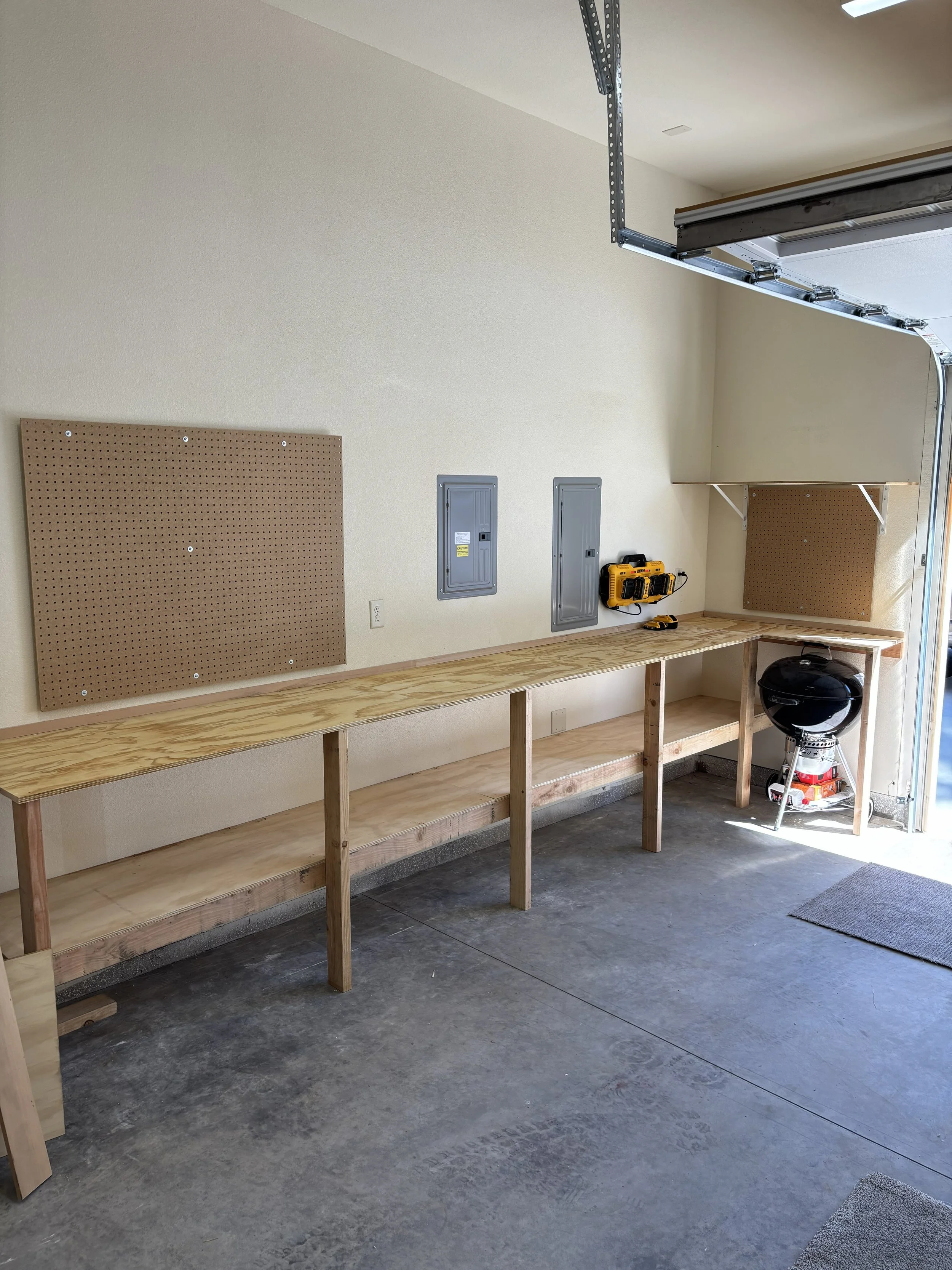 -empty garage with unfinished workbench, pegboard on wall, electrical panels, power drill, grill, and open garage door