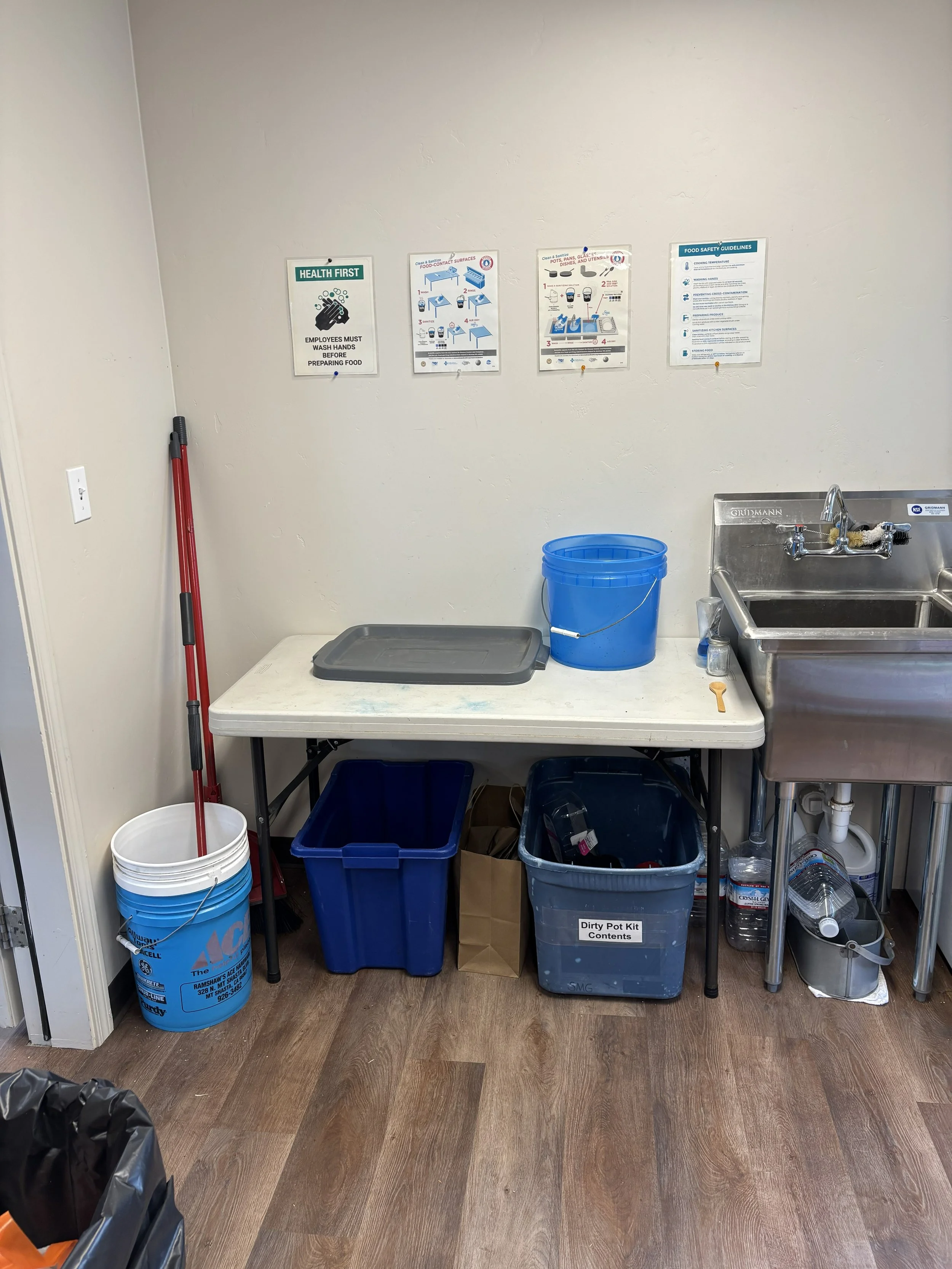 A cleaning station in a workspace with a mop, buckets, a sink, and cleaning supplies on the table.