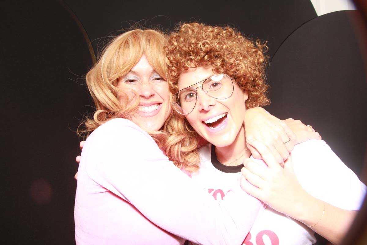 In our custom wooden photo booth, two women in costume, share a warm hug, capturing a fun Halloween moment.