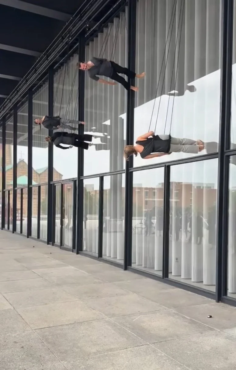 Dancers in harnesses move horizontally across the glass windows of the Neue Nationalgalerie during Trisha Brown’s Walking on the Wall.