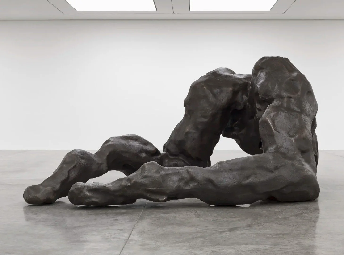 Large dark bronze floor sculpture of a reclining abstracted human figure in a white gallery space at Tate Modern