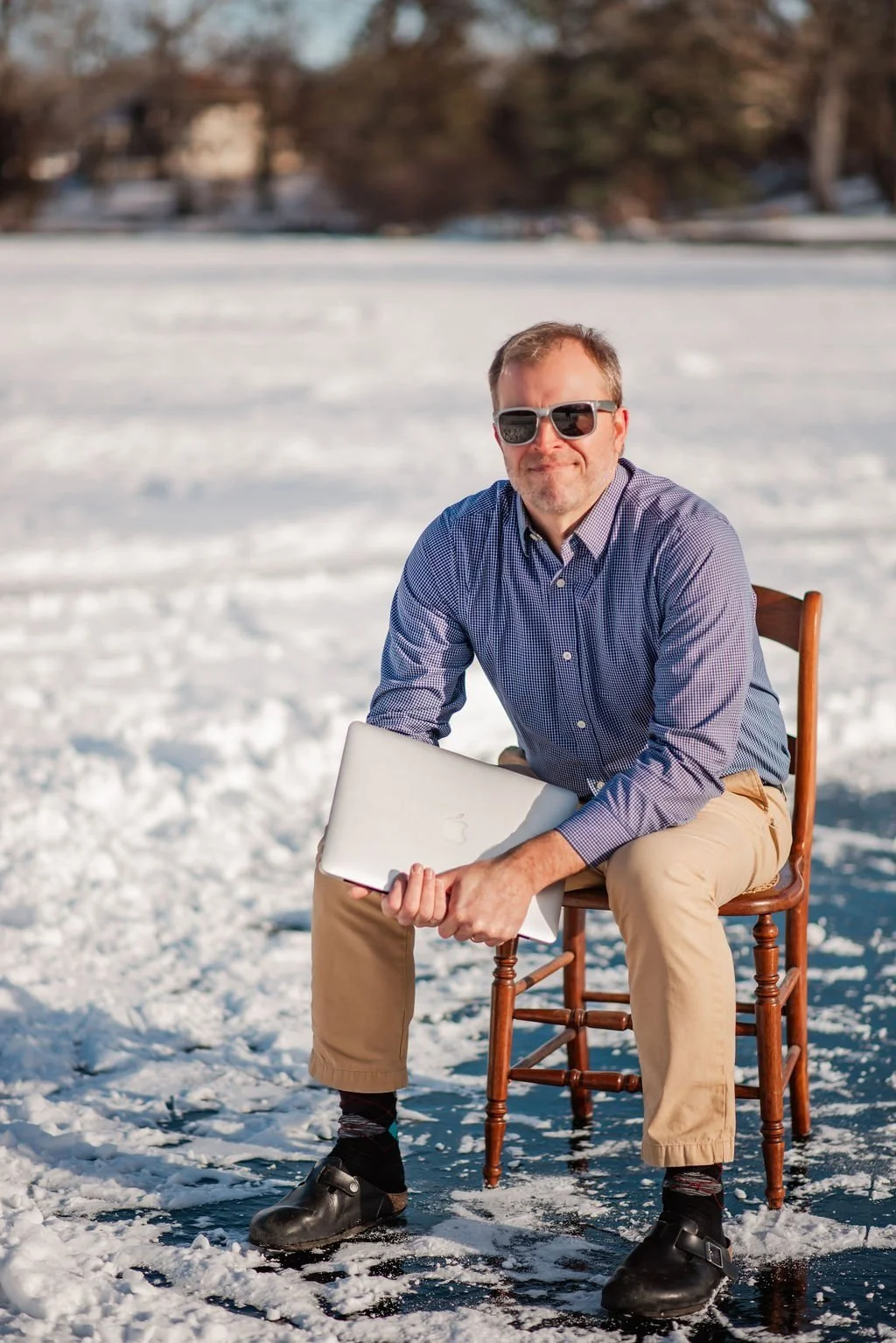 Andy sitting on a wooden chair on the beach in Michigan holding an Apple Macbook Pro