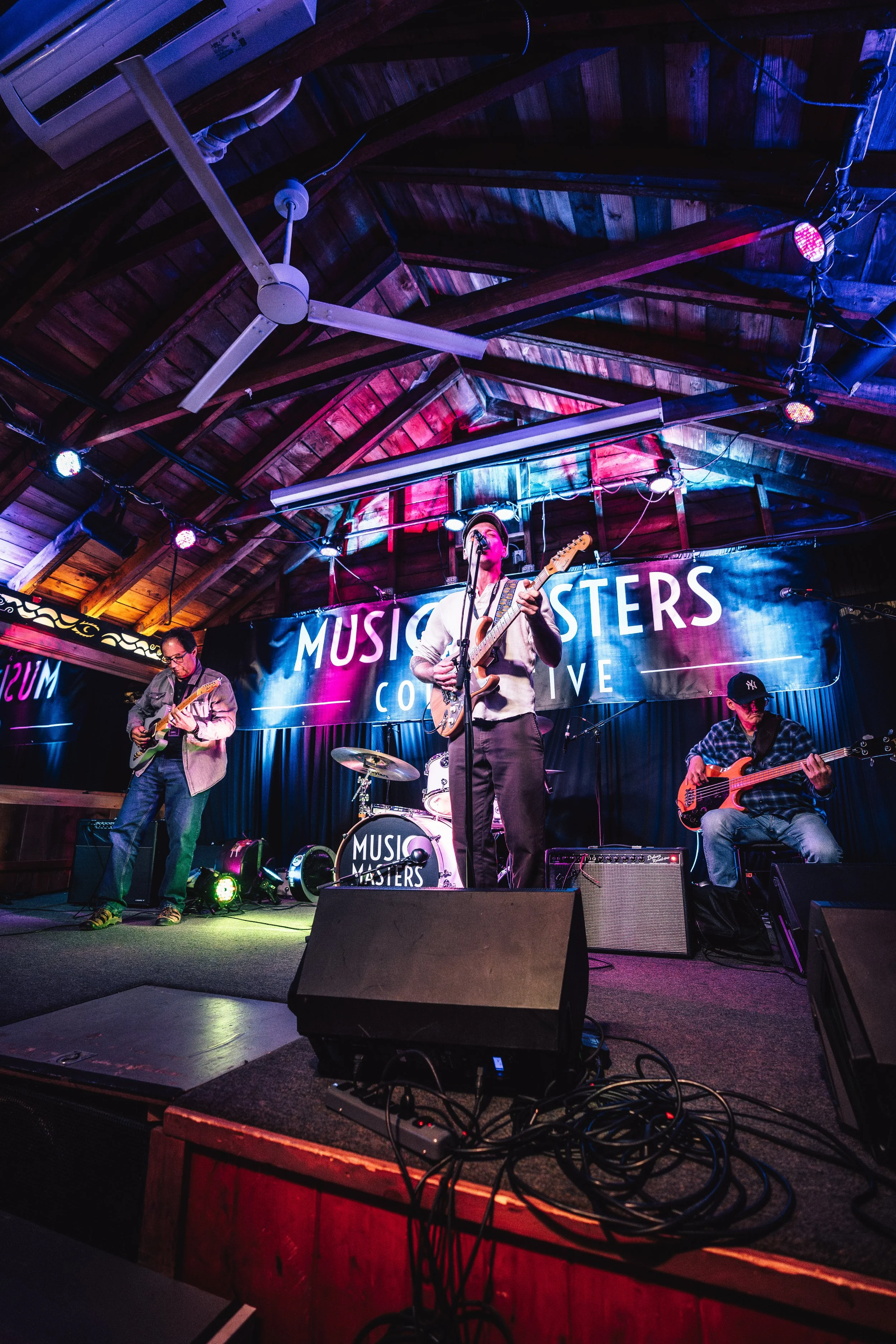 A band called Music Masters performing live on stage in a venue with wooden interior and colorful lighting.