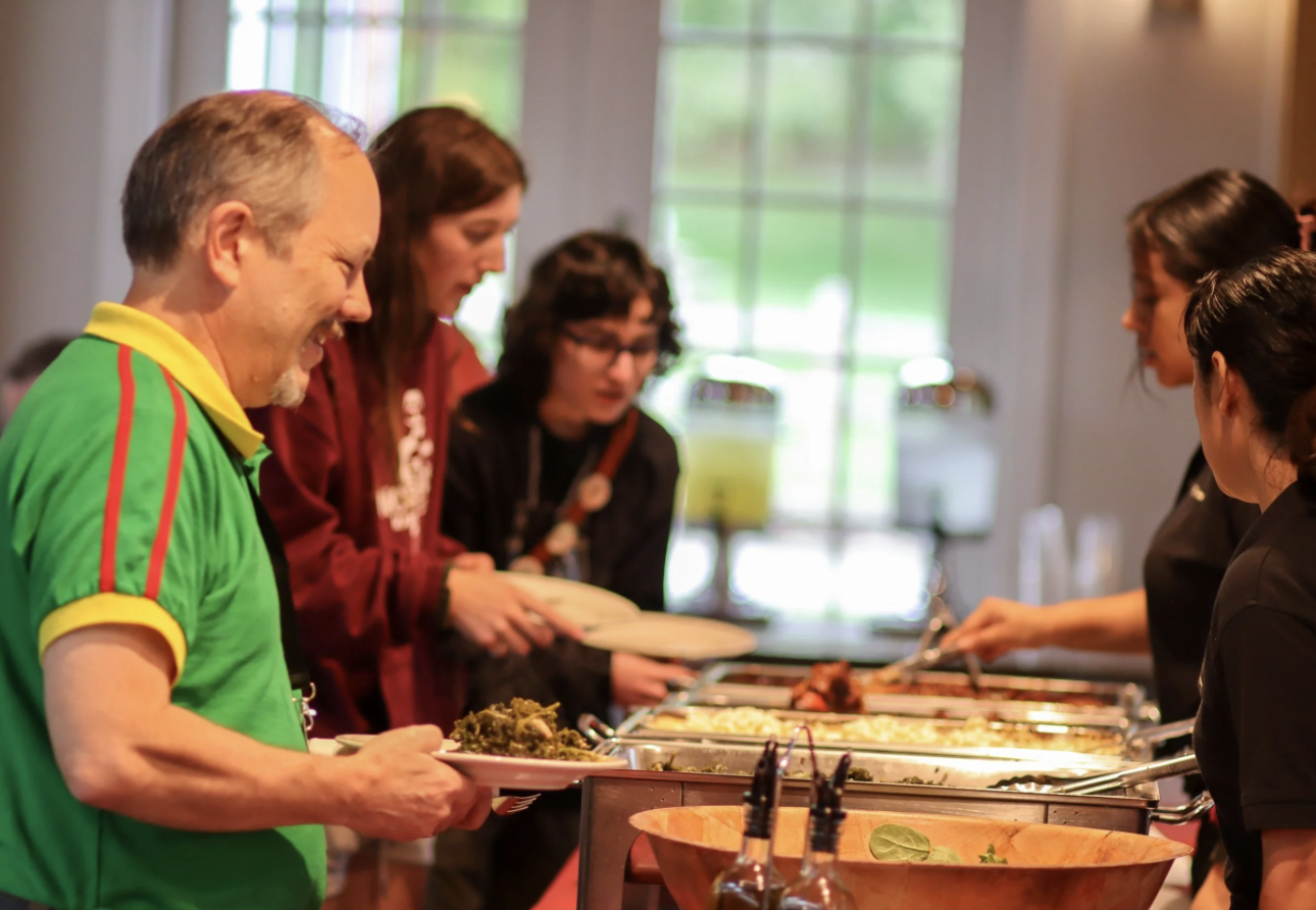 People serving and receiving food at a buffet-style meal in a well-lit dining area.