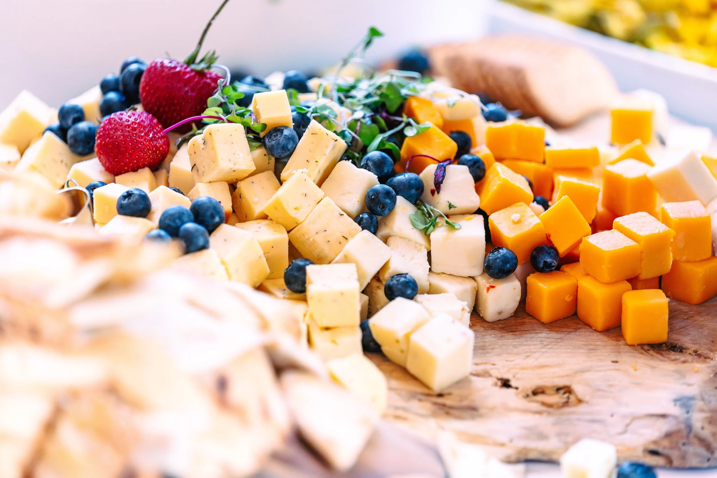 A cheese platter with various types of cheese, blueberries, strawberries, and microgreens on a wooden surface.