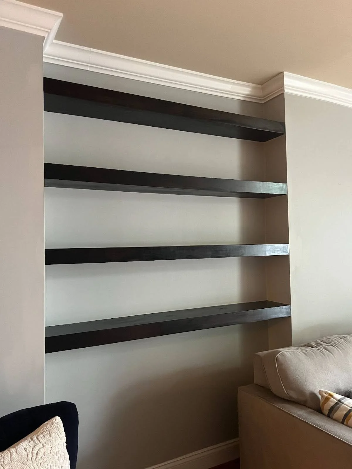 Empty black wooden shelves on a beige wall in a living room.