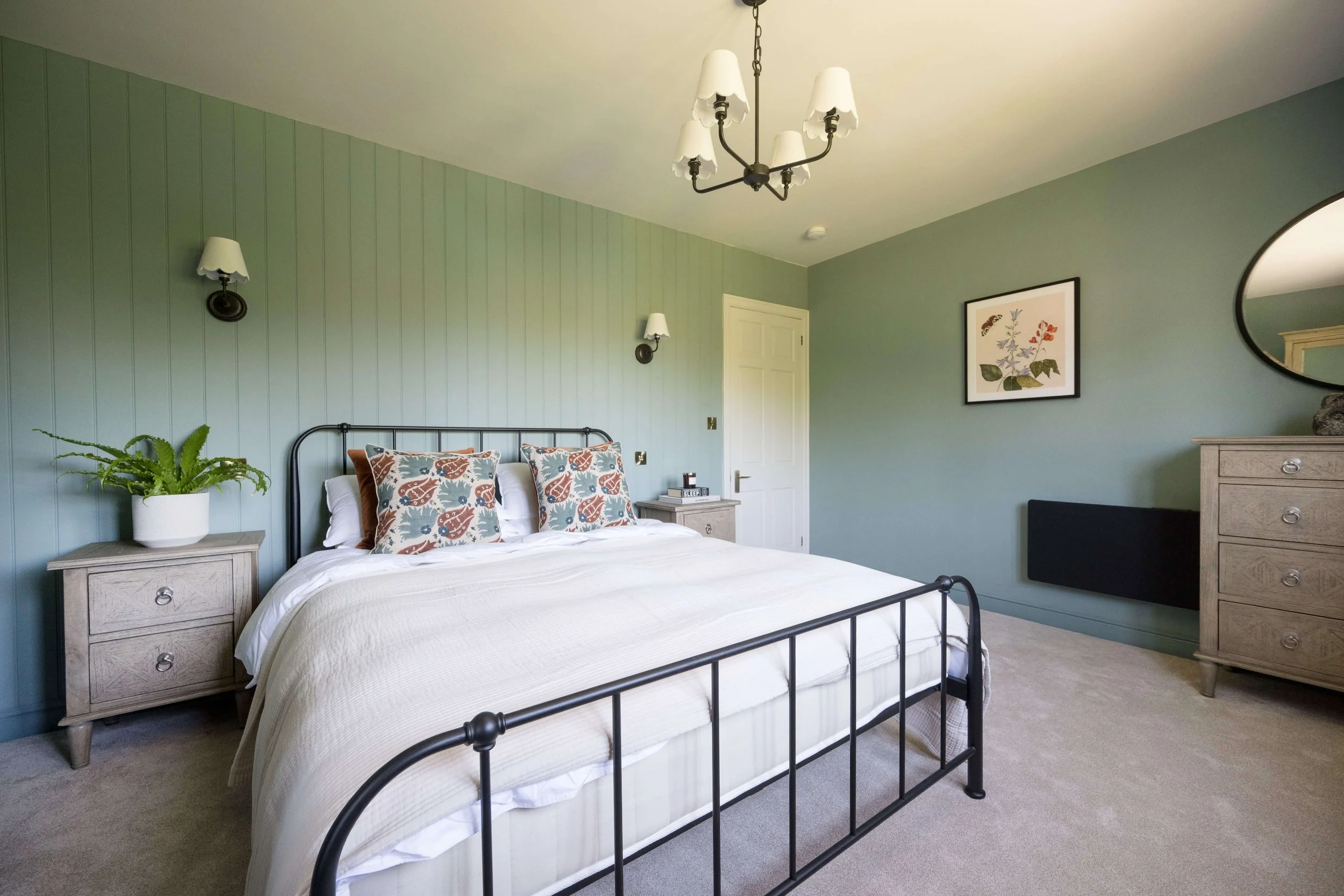 Luxury bedroom by StyleSmith Interiors featuring sage green panelled walls, black metal bed and calming contemporary styling