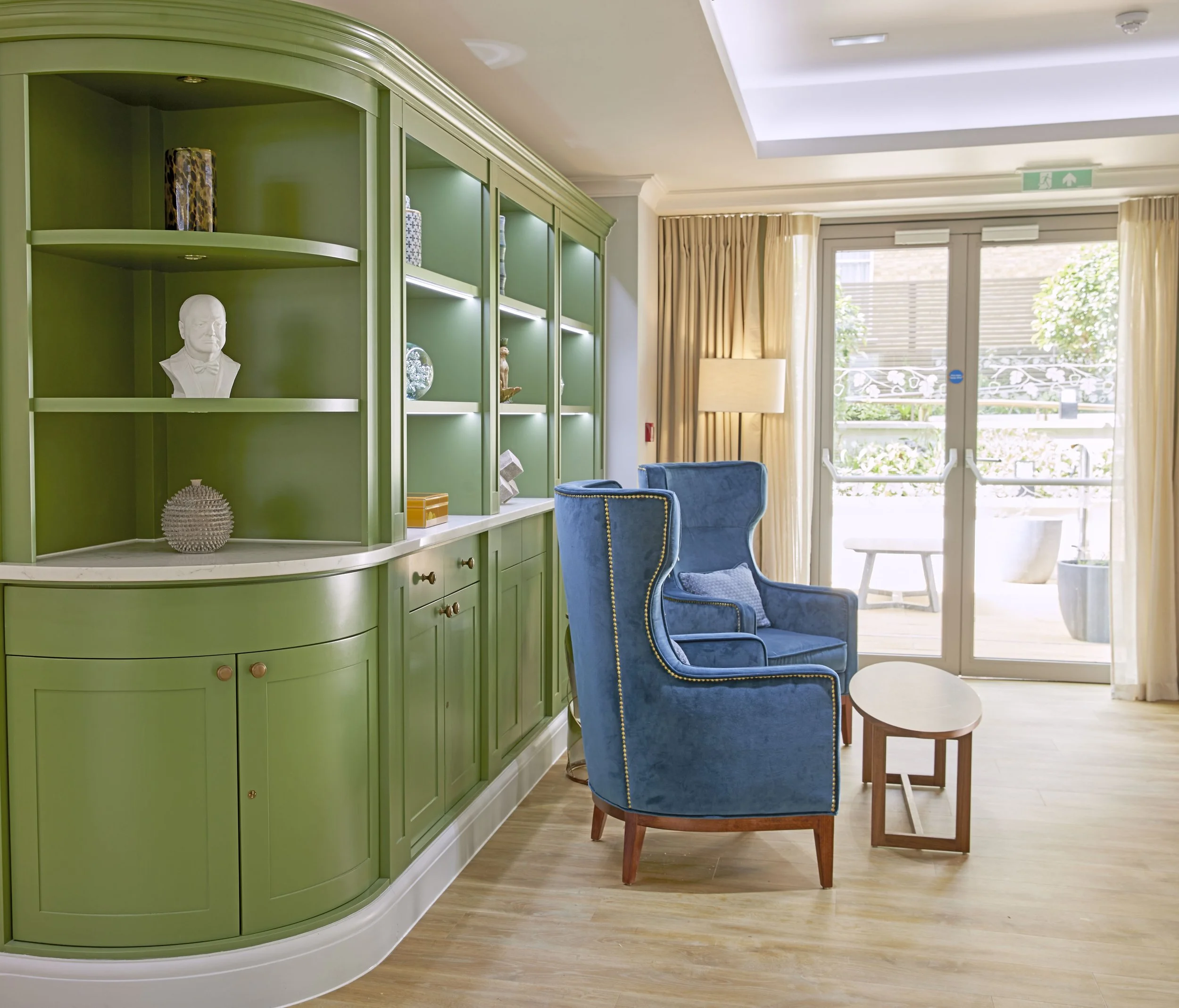 Comfortable seating area within a care home featuring bespoke cabinetry, high-backed lounge chairs and warm, welcoming interiors by StyleSmith Interiors