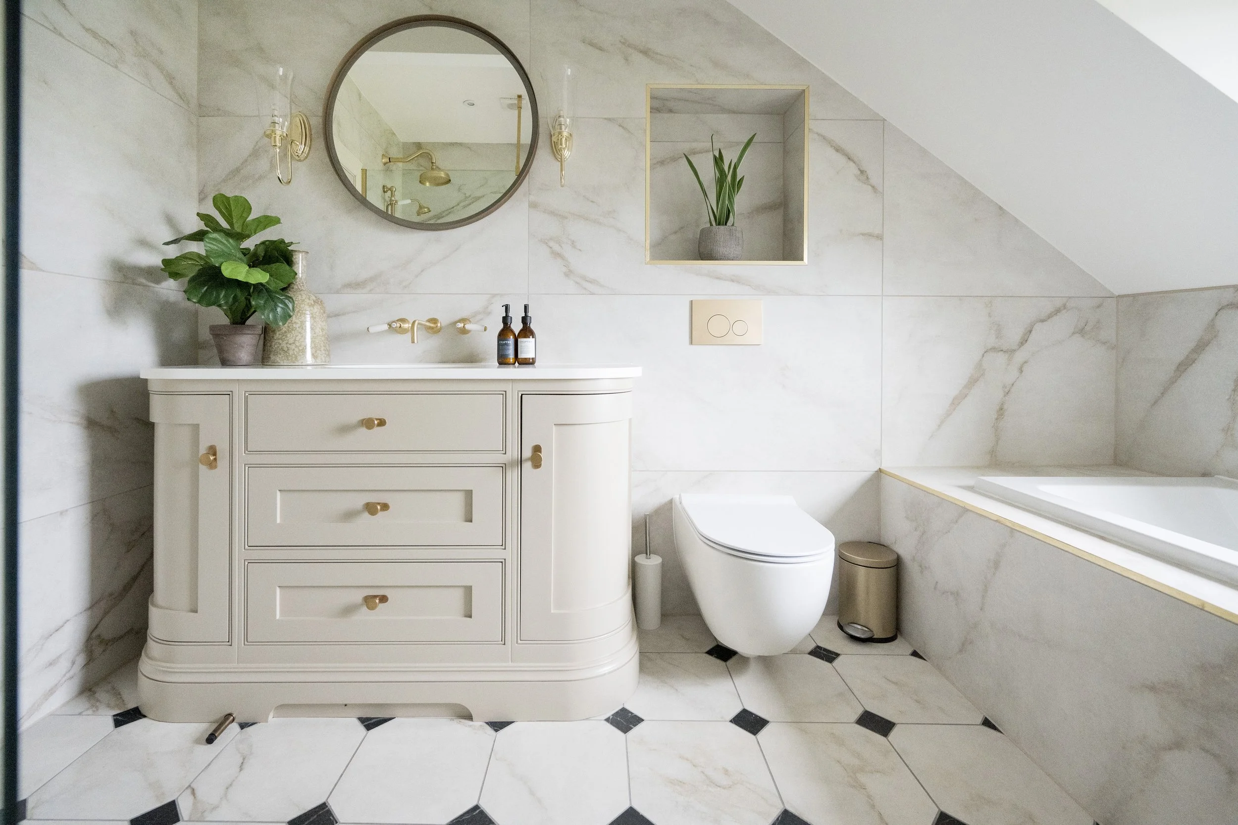 Elegant toilet designed by StyleSmith Interiors with marble-effect wall tiles, bespoke vanity, brass fixtures and built-in shelving in a Yorkshire home