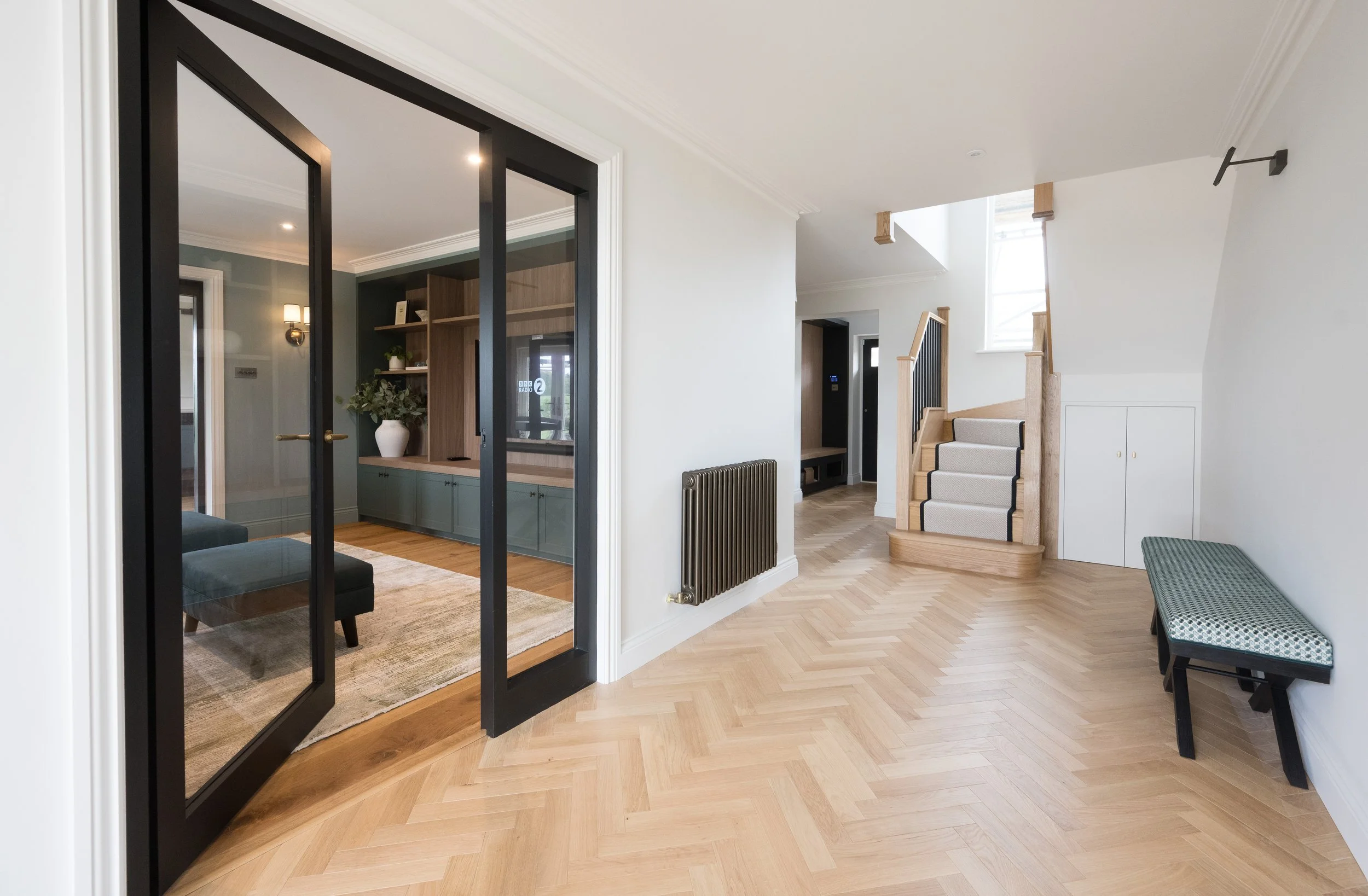 Contemporary hallway by StyleSmith Interiors with herringbone wood flooring, bespoke cabinetry and glazed steel doors in a luxury Harrogate home