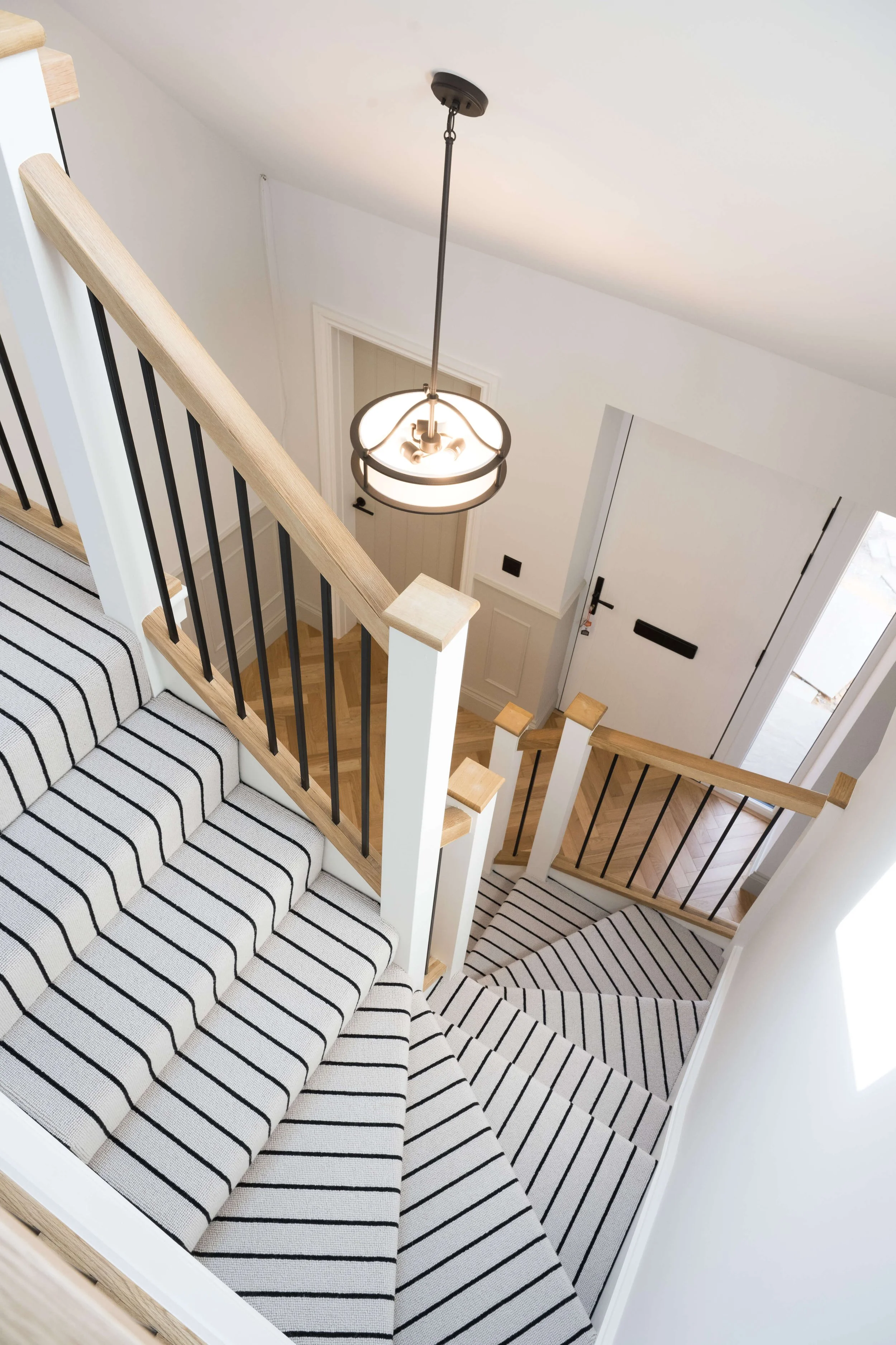 Contemporary staircase with striped carpet runner, oak handrail and black balustrades designed by StyleSmith Interiors for Property Developers