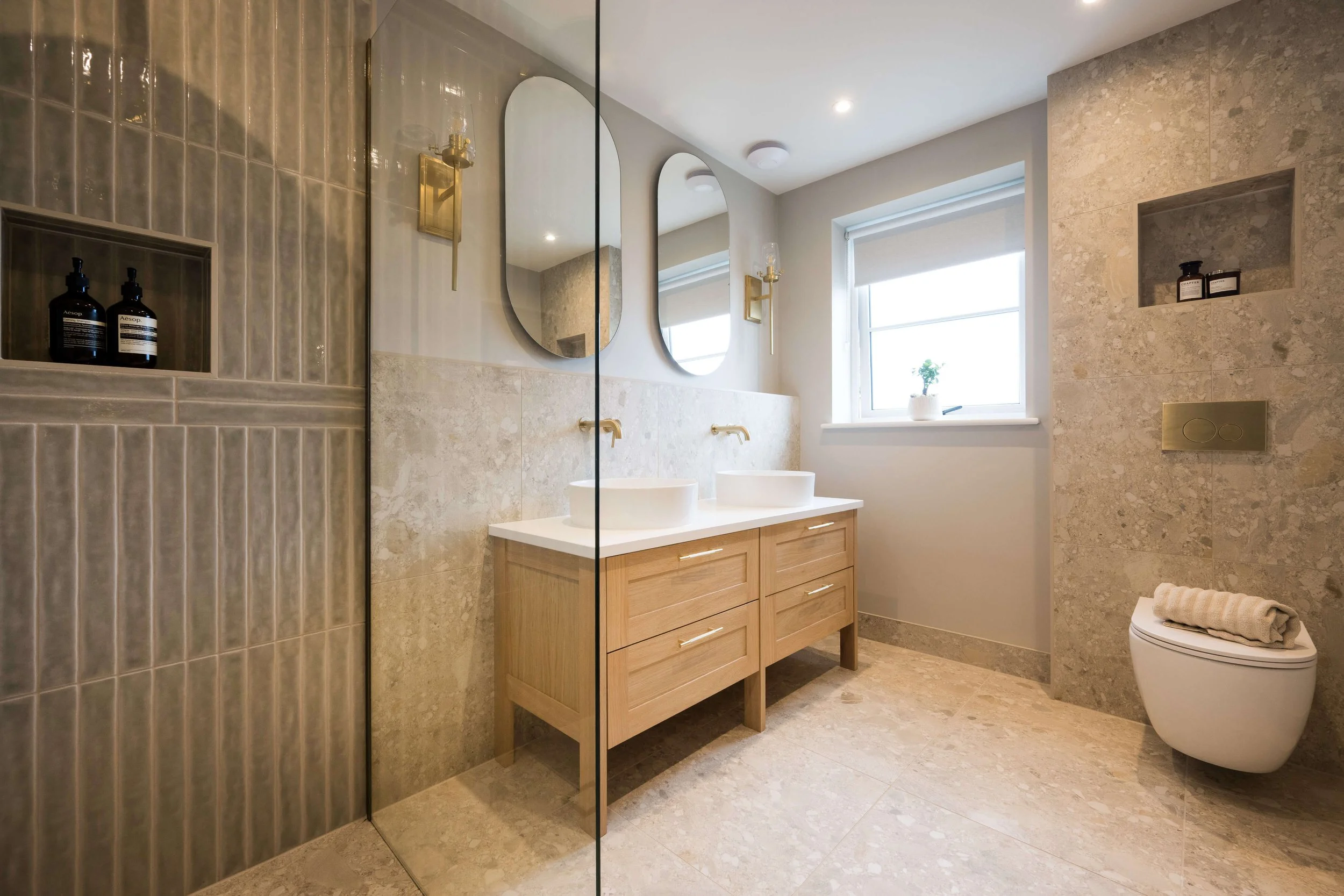 Contemporary bathroom with an oak vanity unit, vessel basins, marble wall tiles and brushed brass taps designed by StyleSmith Interiors