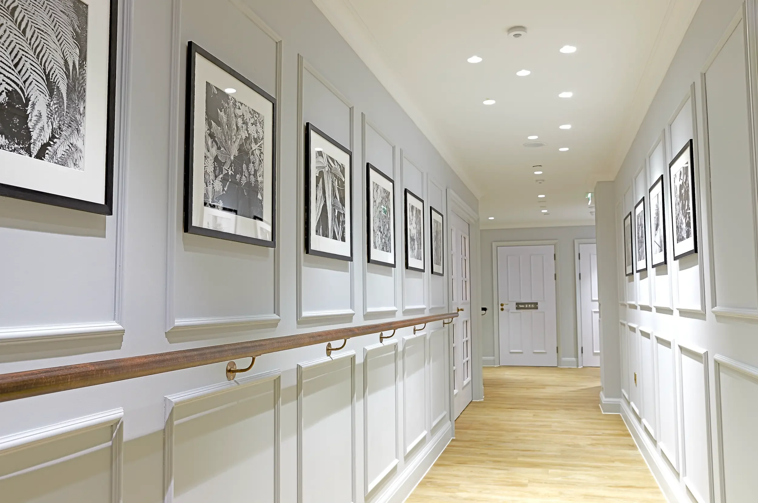 Wide care home corridor with decorative wall panelling, artwork, handrails and accessible design by StyleSmith Interiors