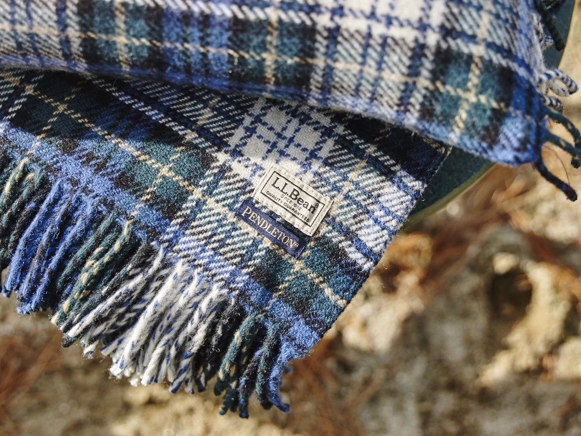 Close-up of a plaid scarf with tags labeled LL Bean and Pendleton, featuring fringe edges.