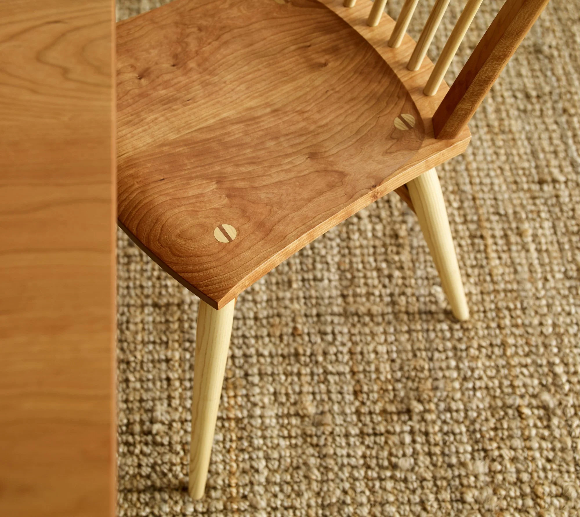 Close-up of a wooden chair with a curved seat and light-colored legs, placed on a textured beige carpet.