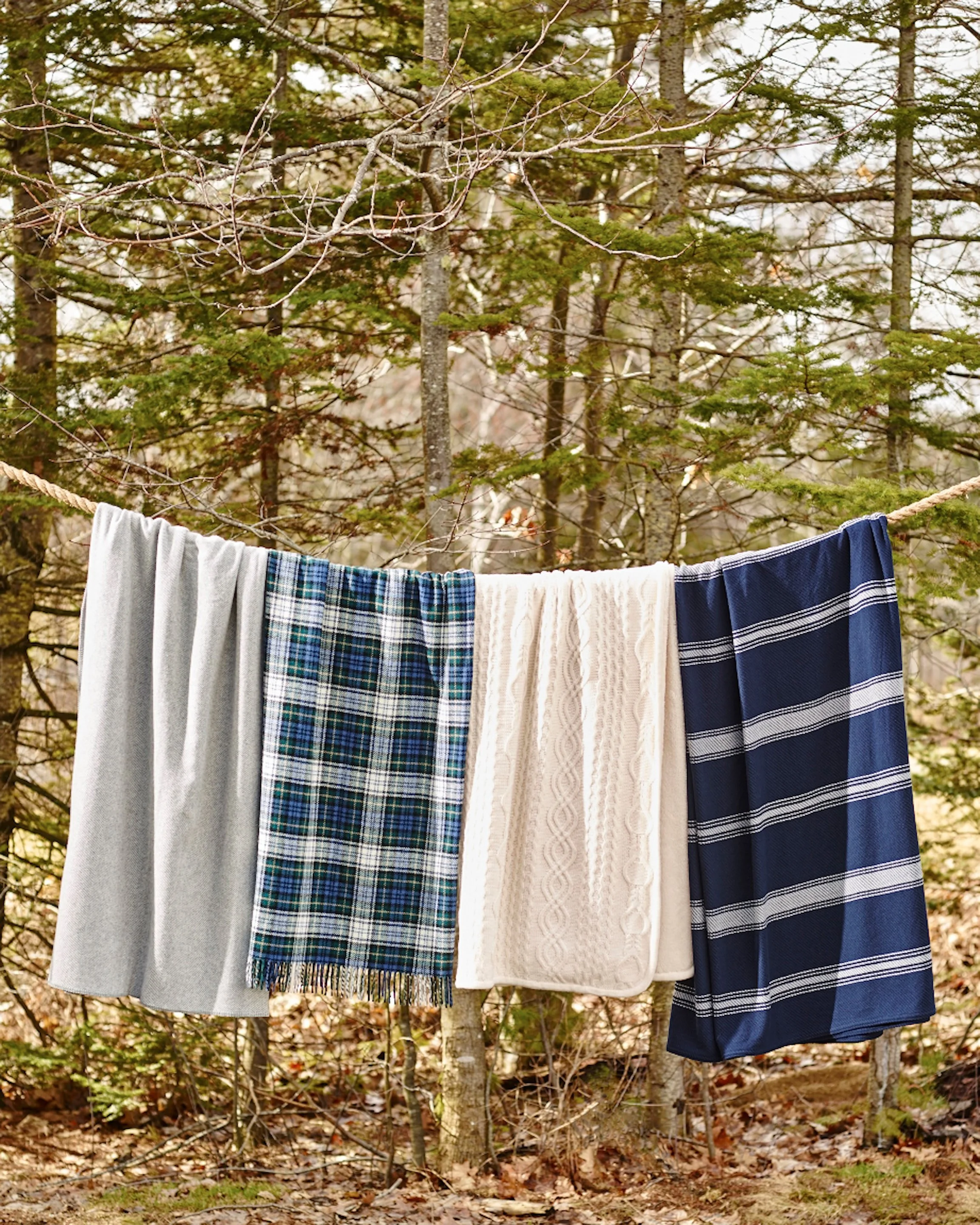 Clothes hanging on a clothesline in front of a wooded area with trees and fallen leaves