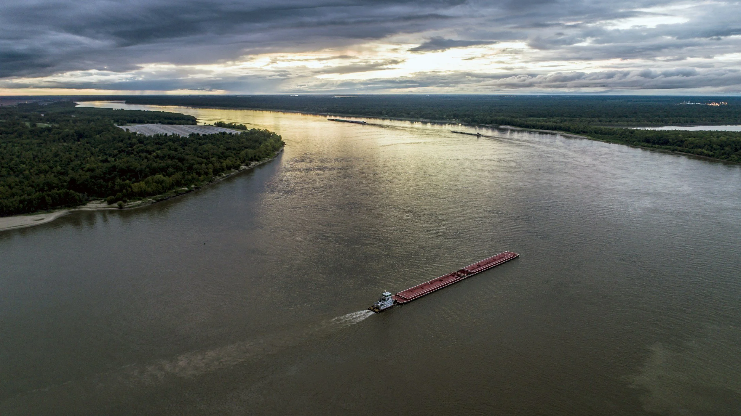 An aerial view of the Mississippi River with a barge traveling on the water during the day with overcast skies.
