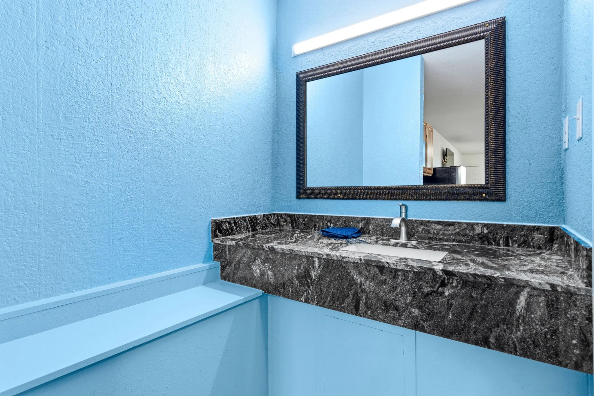 Bathroom vanity with black and white marble countertop, blue walls, a large mirror, and a light fixture above the mirror.