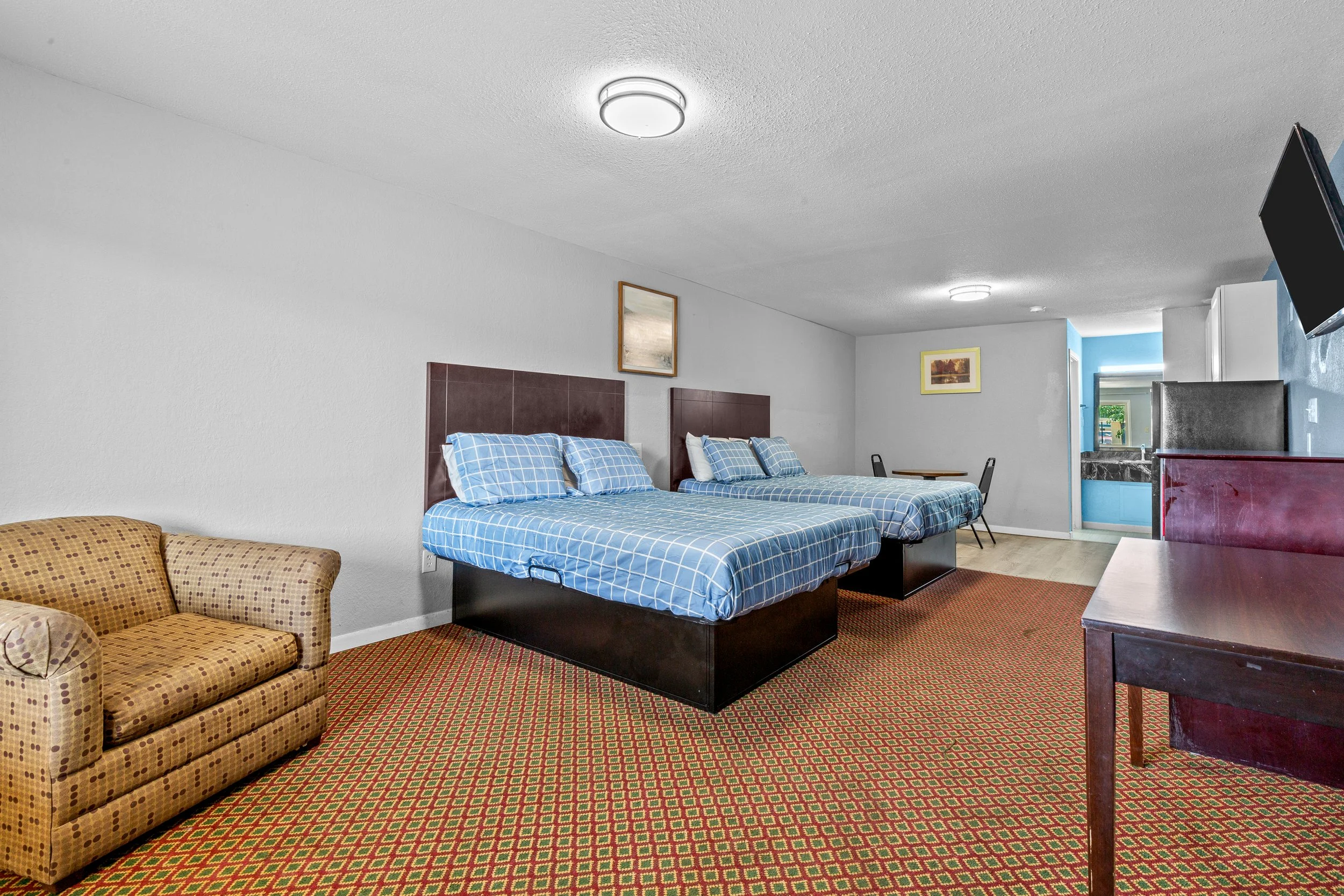 Interior of a hotel room with two beds, a sofa, a TV mounted on the wall, and artwork on the walls.